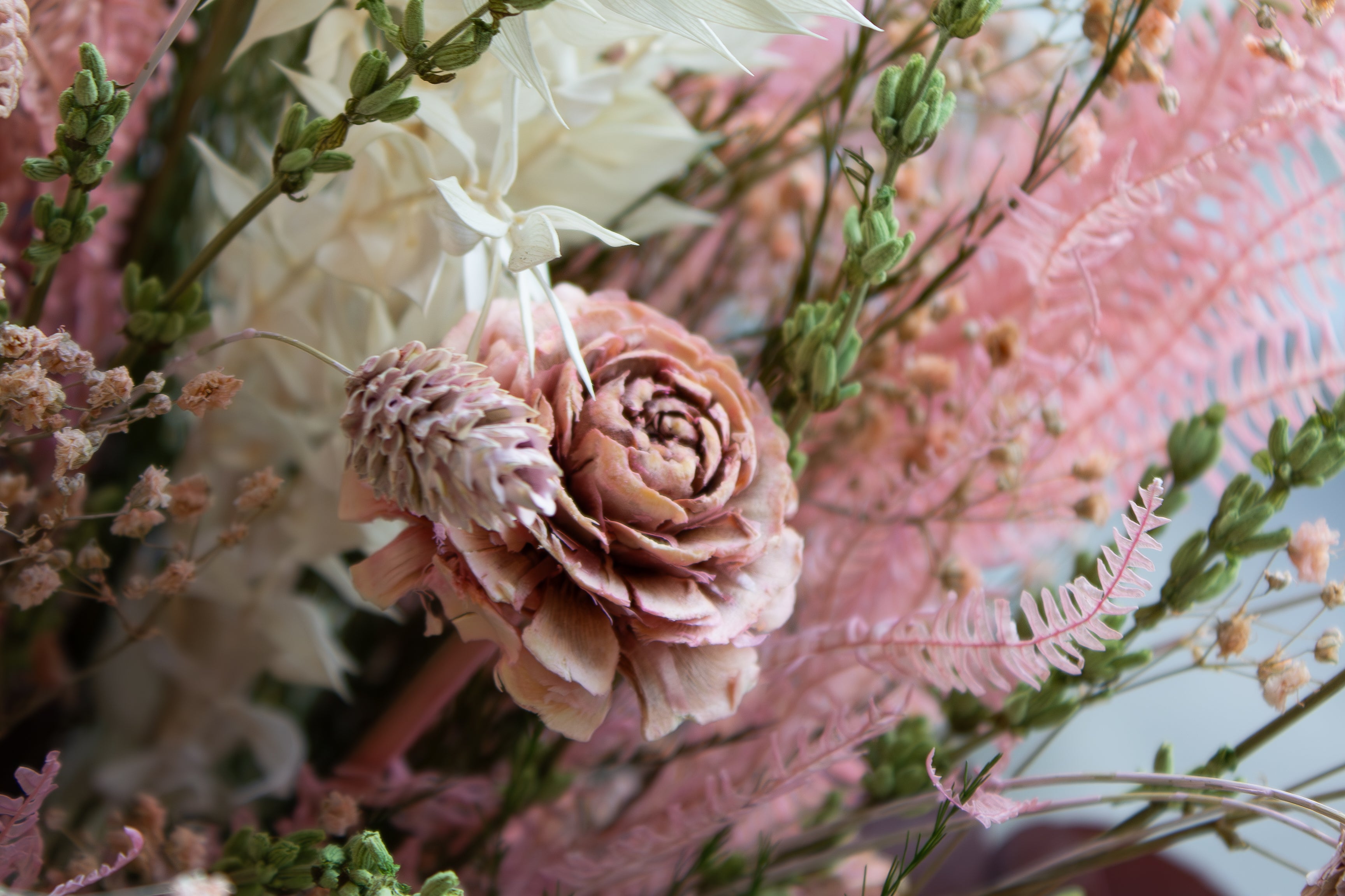 Nærbillede af en blomsterbuket med langtidsholdbare blomster i sarte lyserøde nuancer.