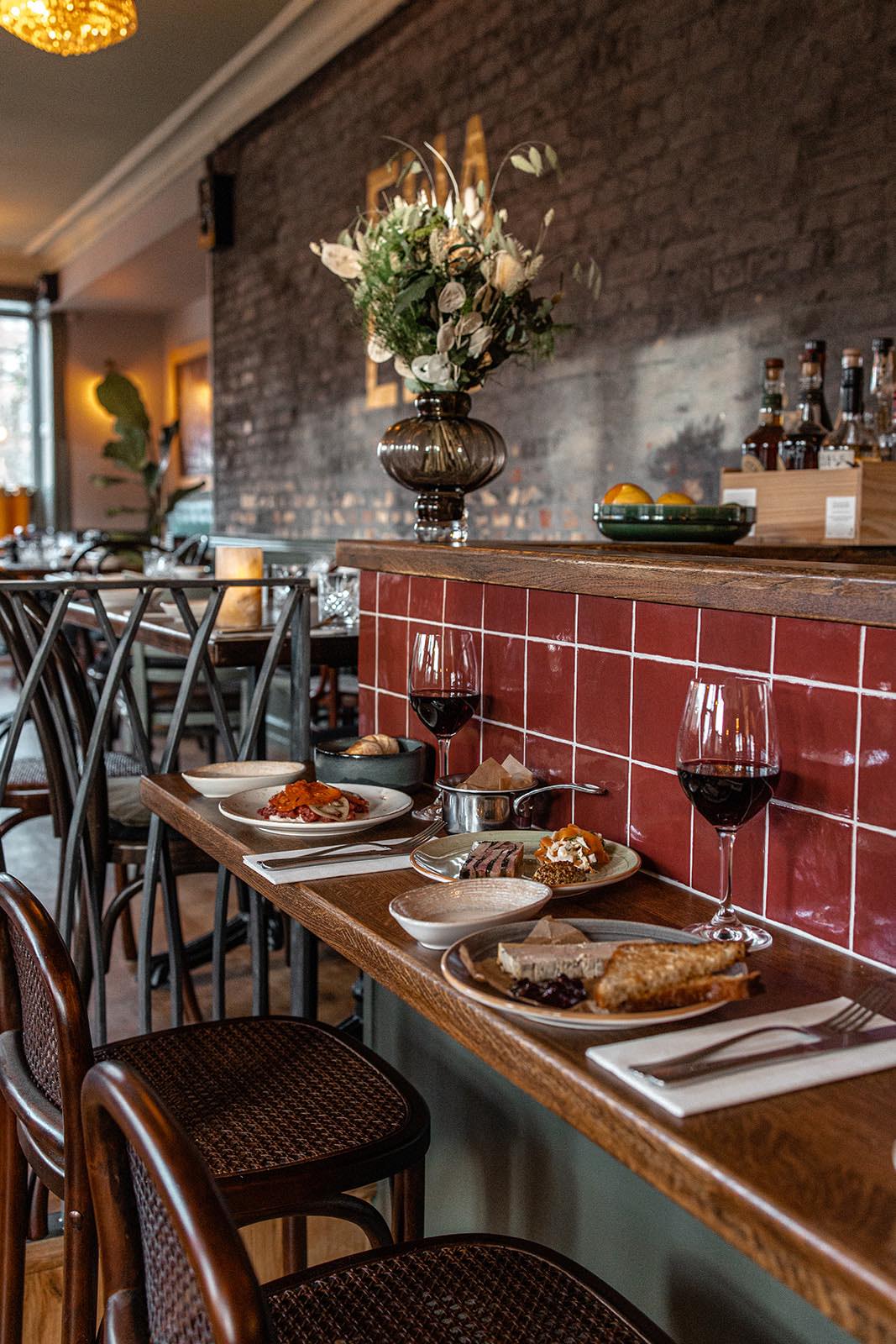 På bardisken i en smagfuldt indrettet restaurant står en grøn-hvid blomsterbuket i en buet vase.