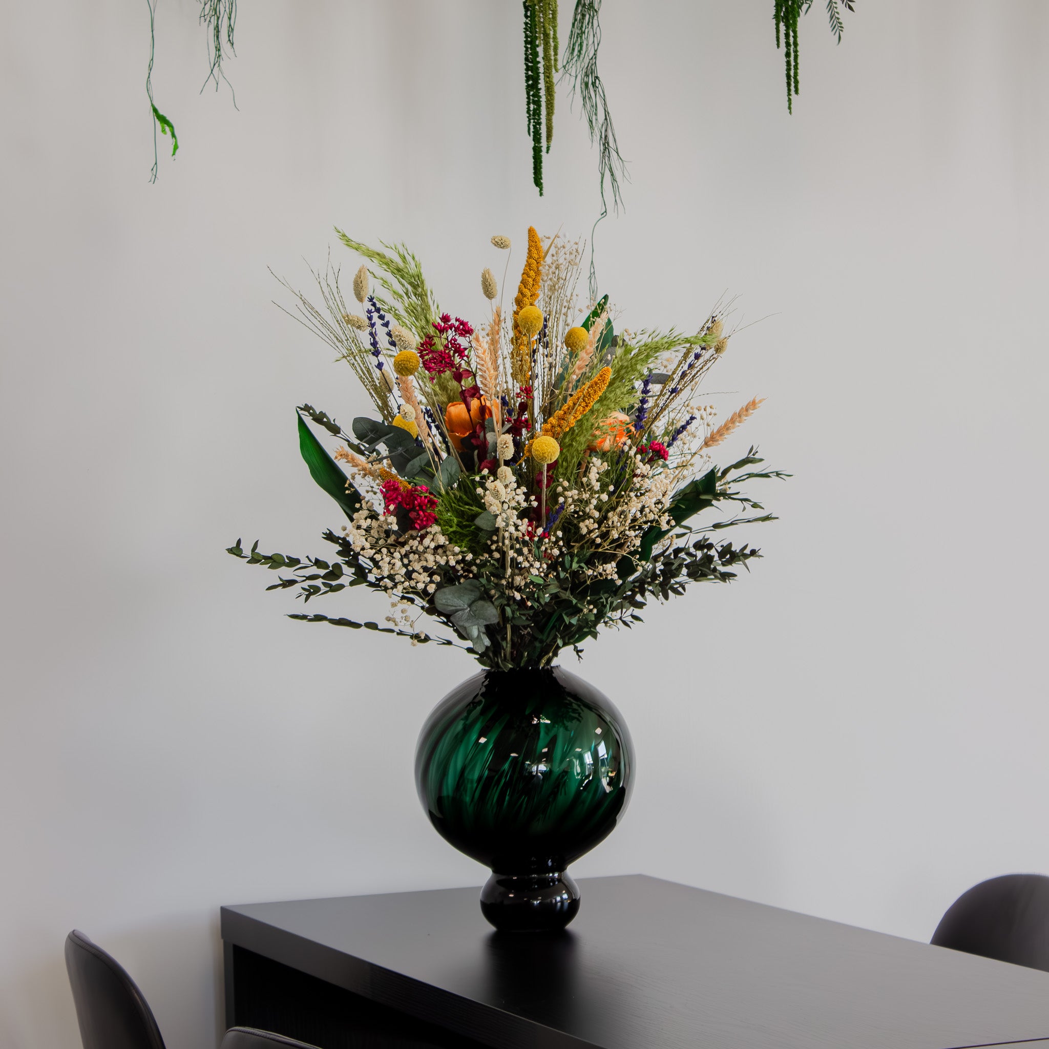 Sommerlig, naturlig bukket med langtidsholdbare blomster står i en grøn, buet vase på et bord.