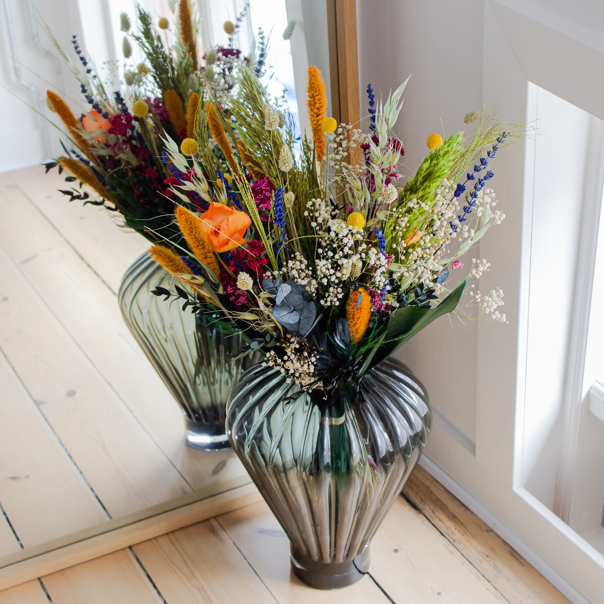 I et hjørne foran et spejl står en farverig buket i en glasvase.