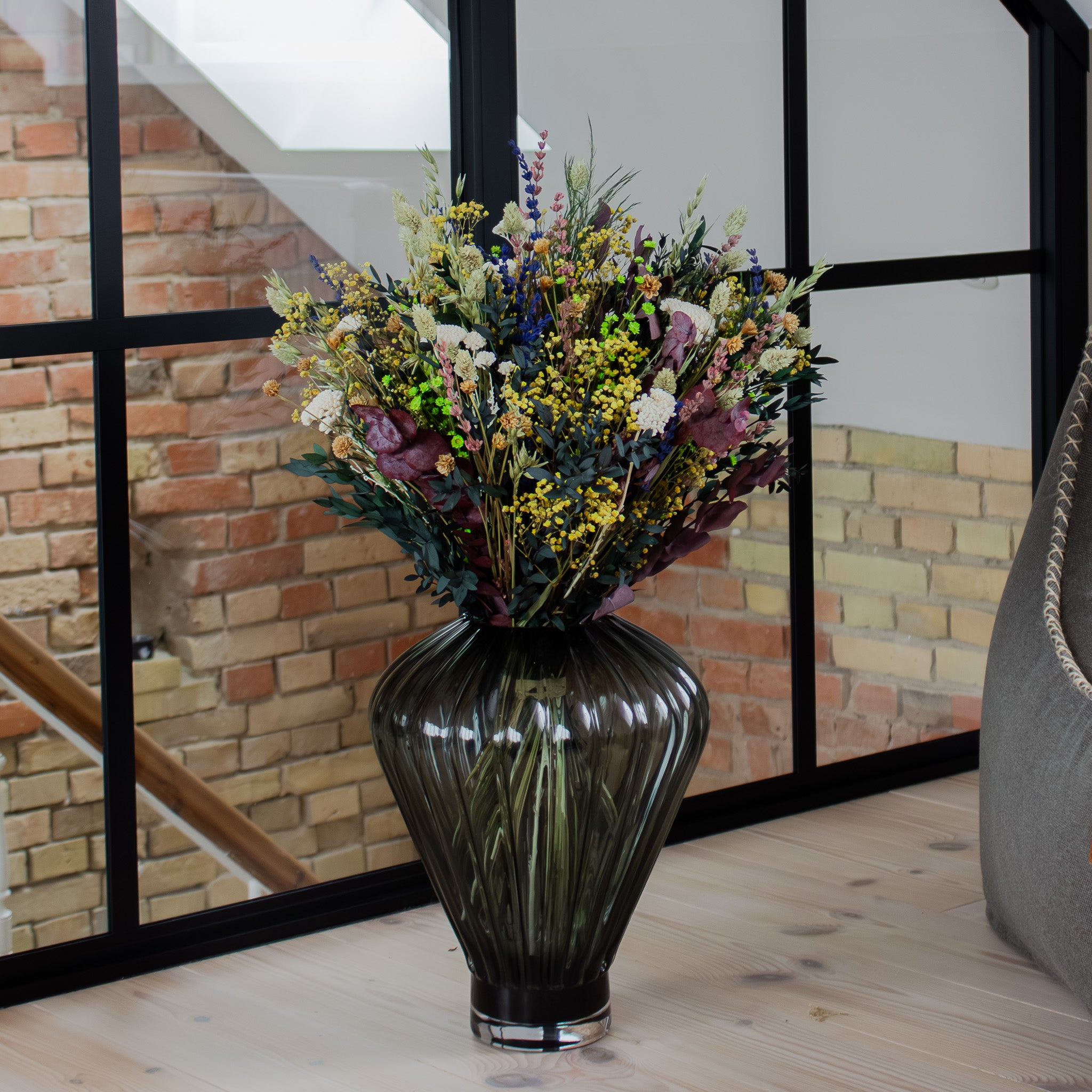 I et hjørne af et rum står en stor geometrisk glasvase med en farverig blomsterbuket.