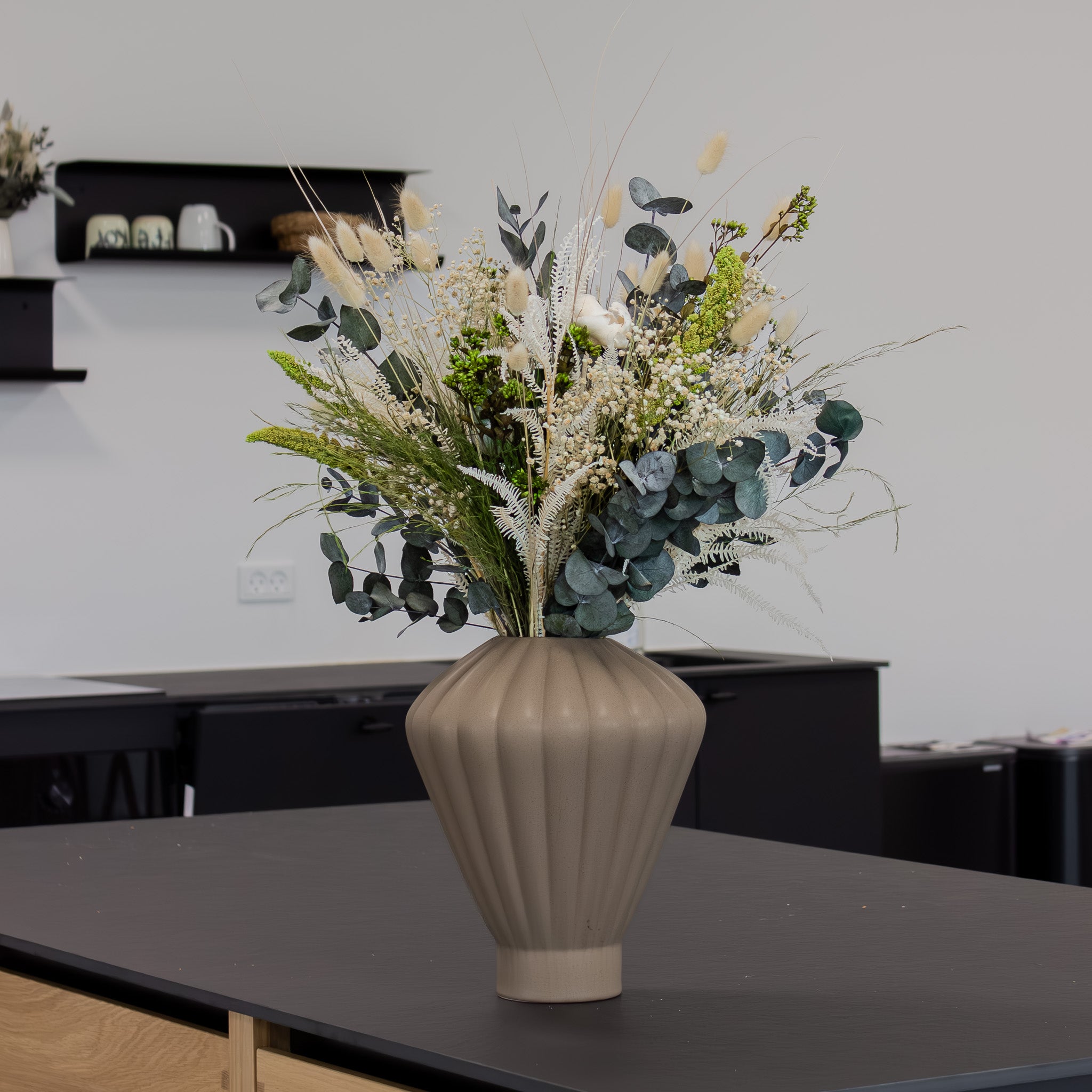 På et bord står en geometrisk, lysebrun vase med en grøn-hvid blomsterbuket.