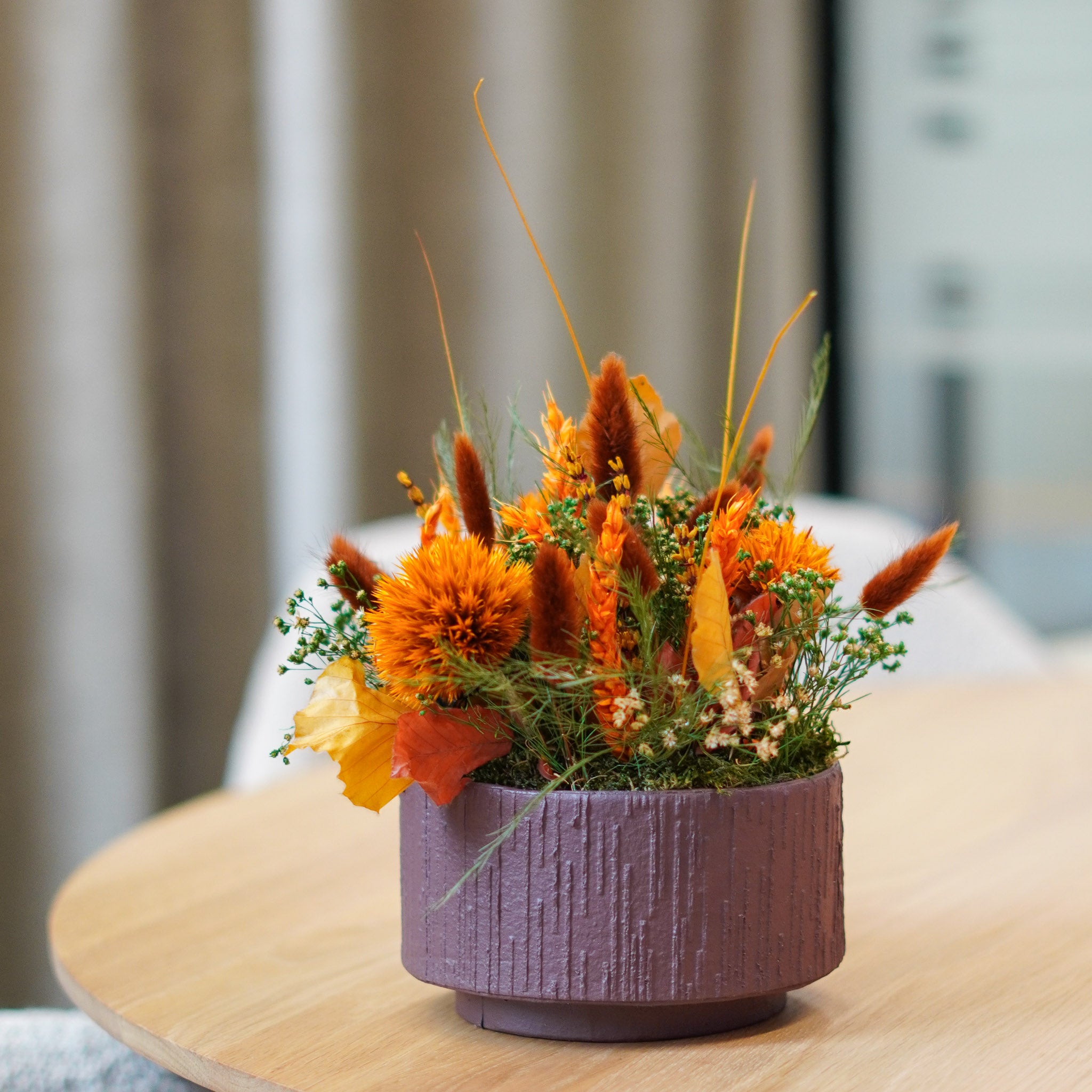 I en papbakke er langtidsholdbare blomster i kraftige orange nuancer arrangeret.