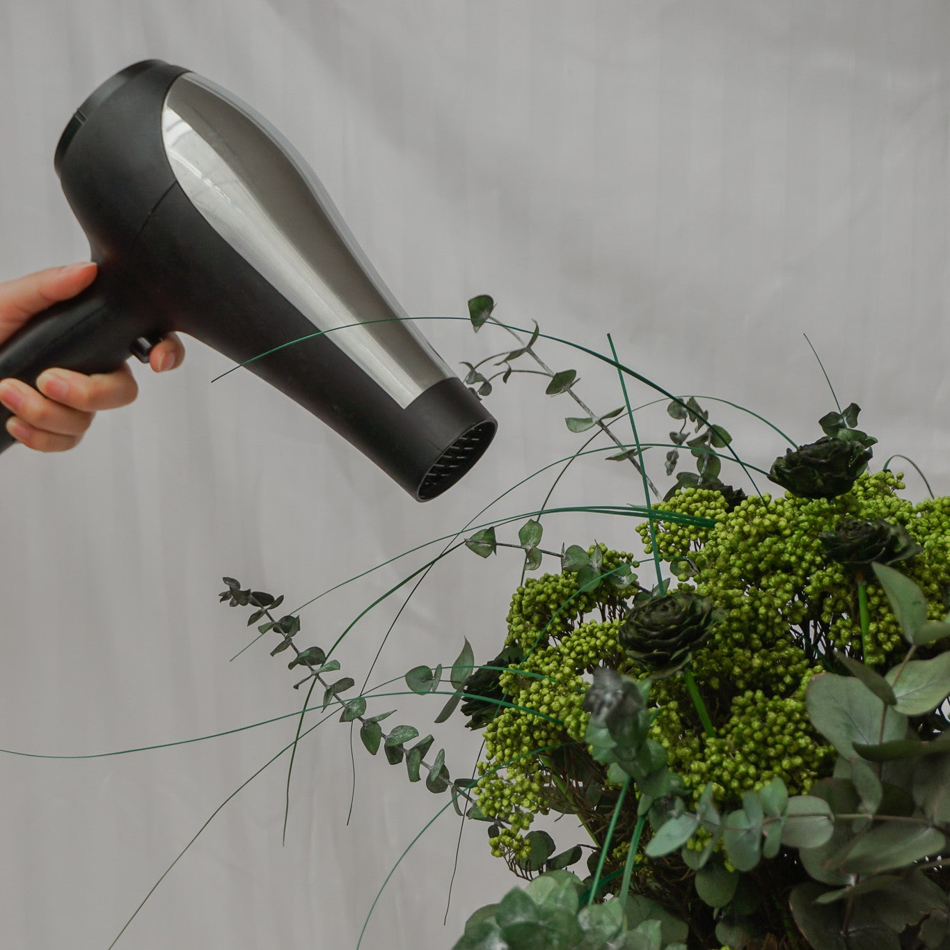 En hårtørrer er rettet mod en grøn blomsterbuket.