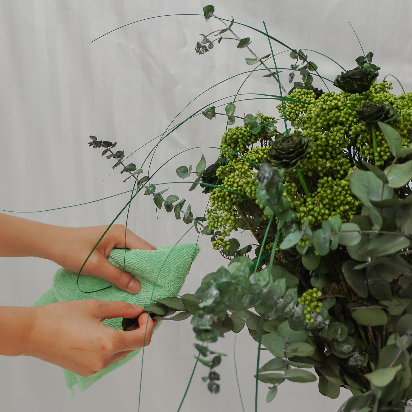 Eukalyptusbladene på en grøn blomsterbuket tørres forsigtigt af med en mikrofiberklud.