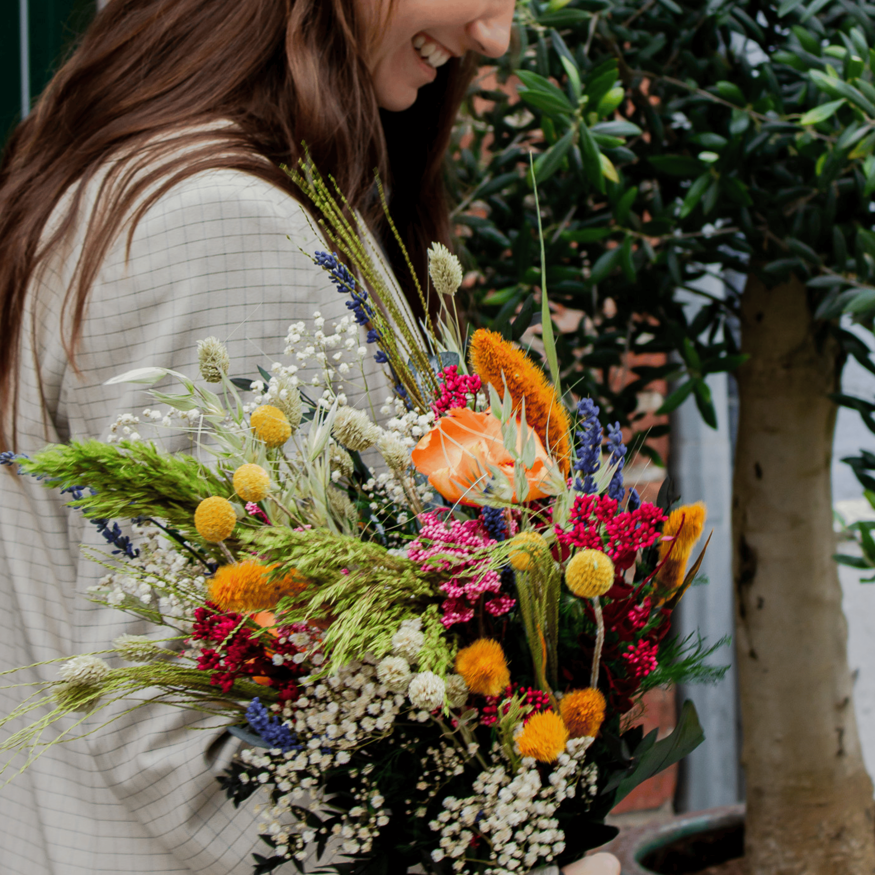 En smilende kvinde holder en farverig blomsterbuket i hånden.
