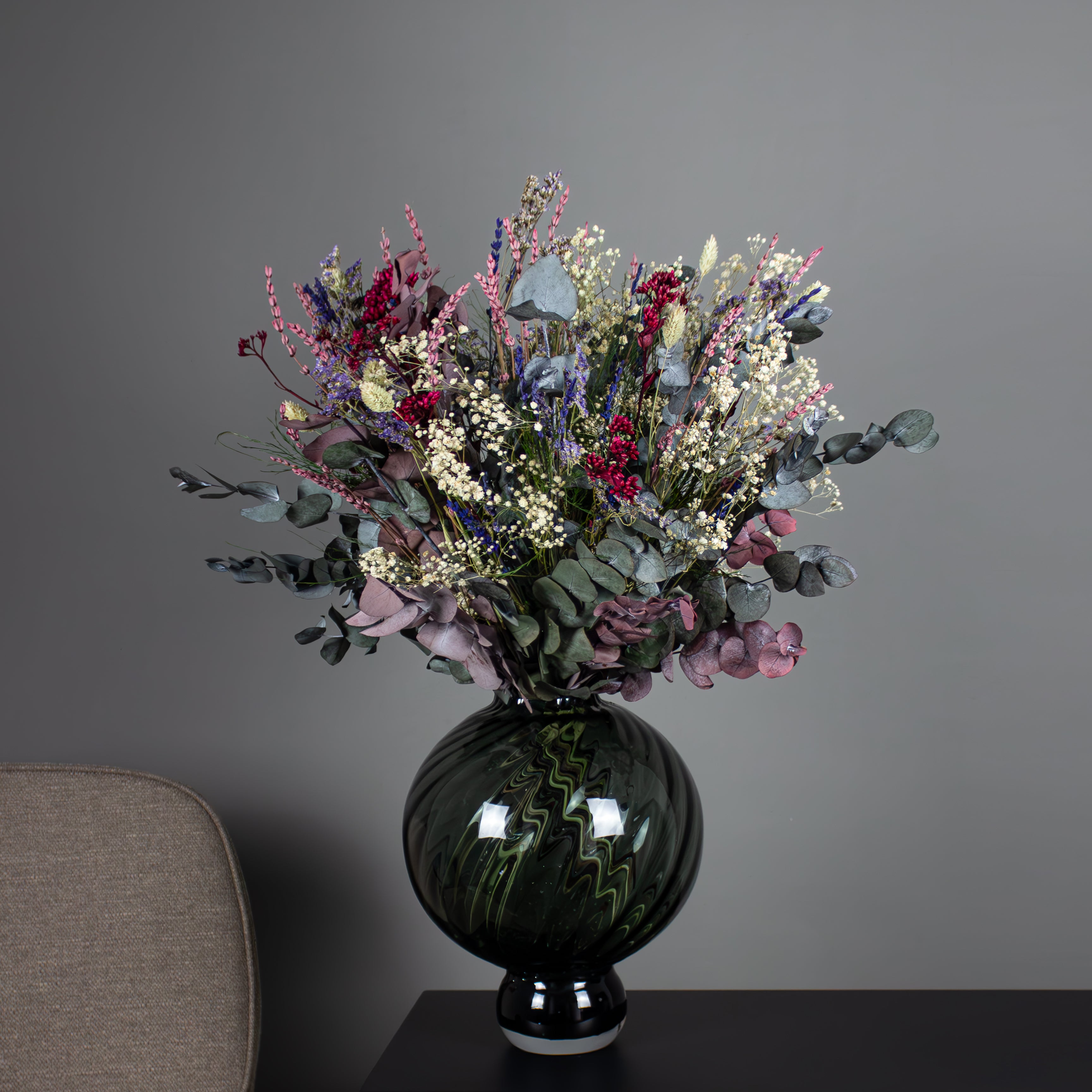 I en buet vase står en vild buket med violette, blå og røde accenter.