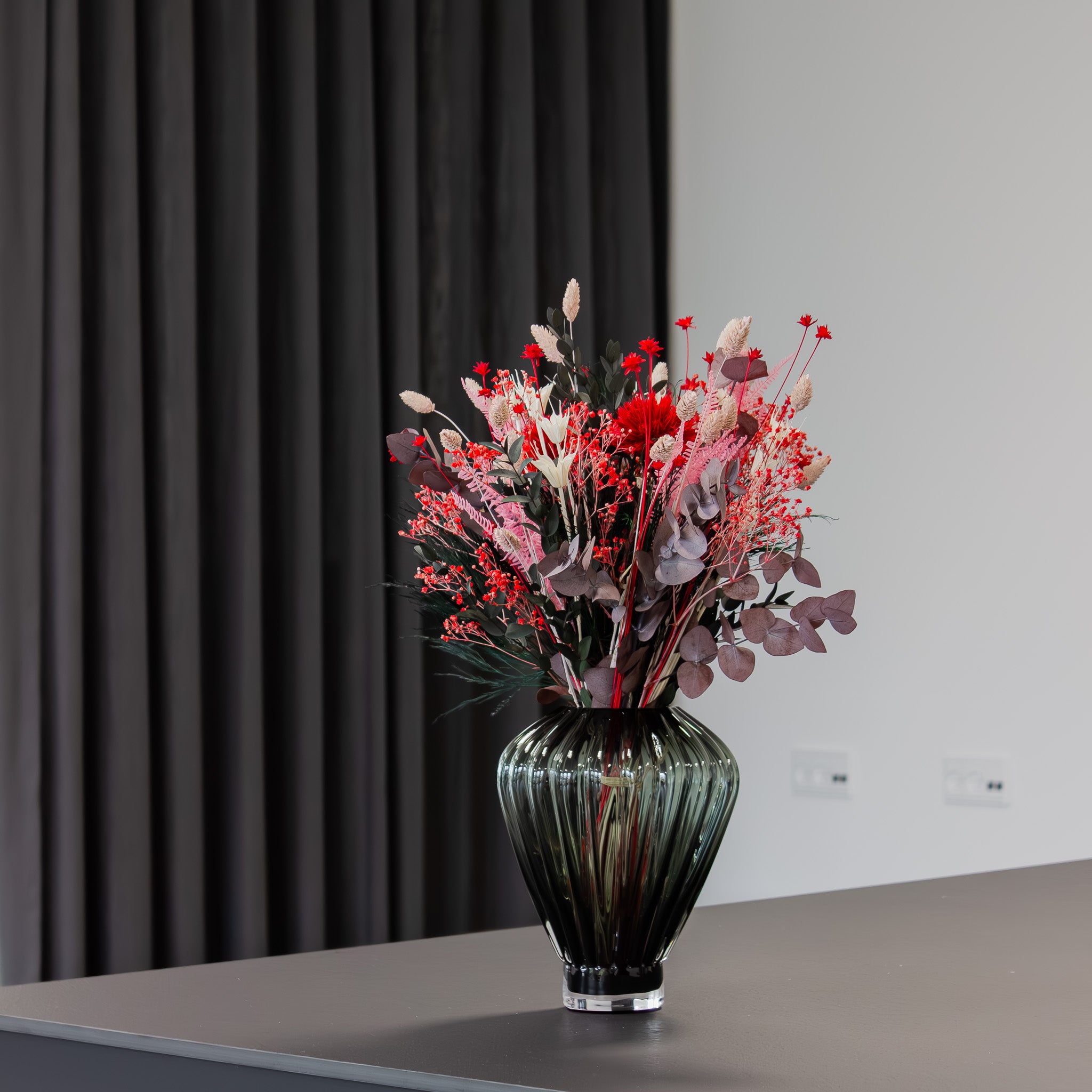 I en rillede glasvase står en blomsterbuket i stærke rød-pink nuancer.