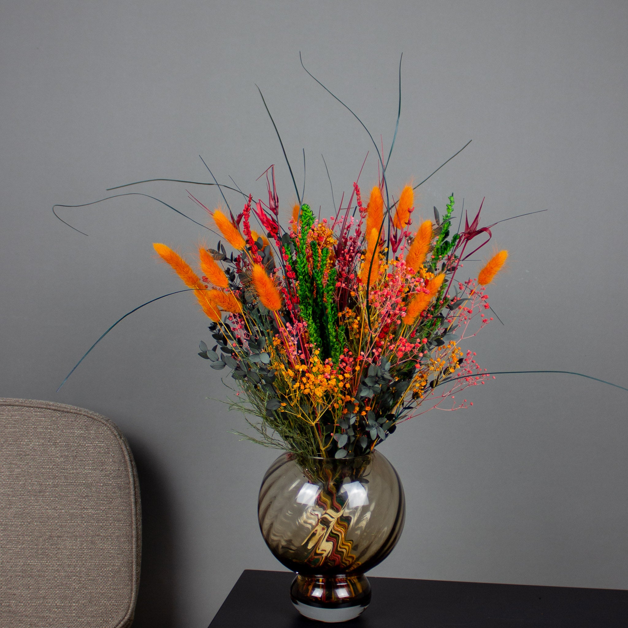 En buket i kraftige orange og røde nuancer står i en rund glasvase.