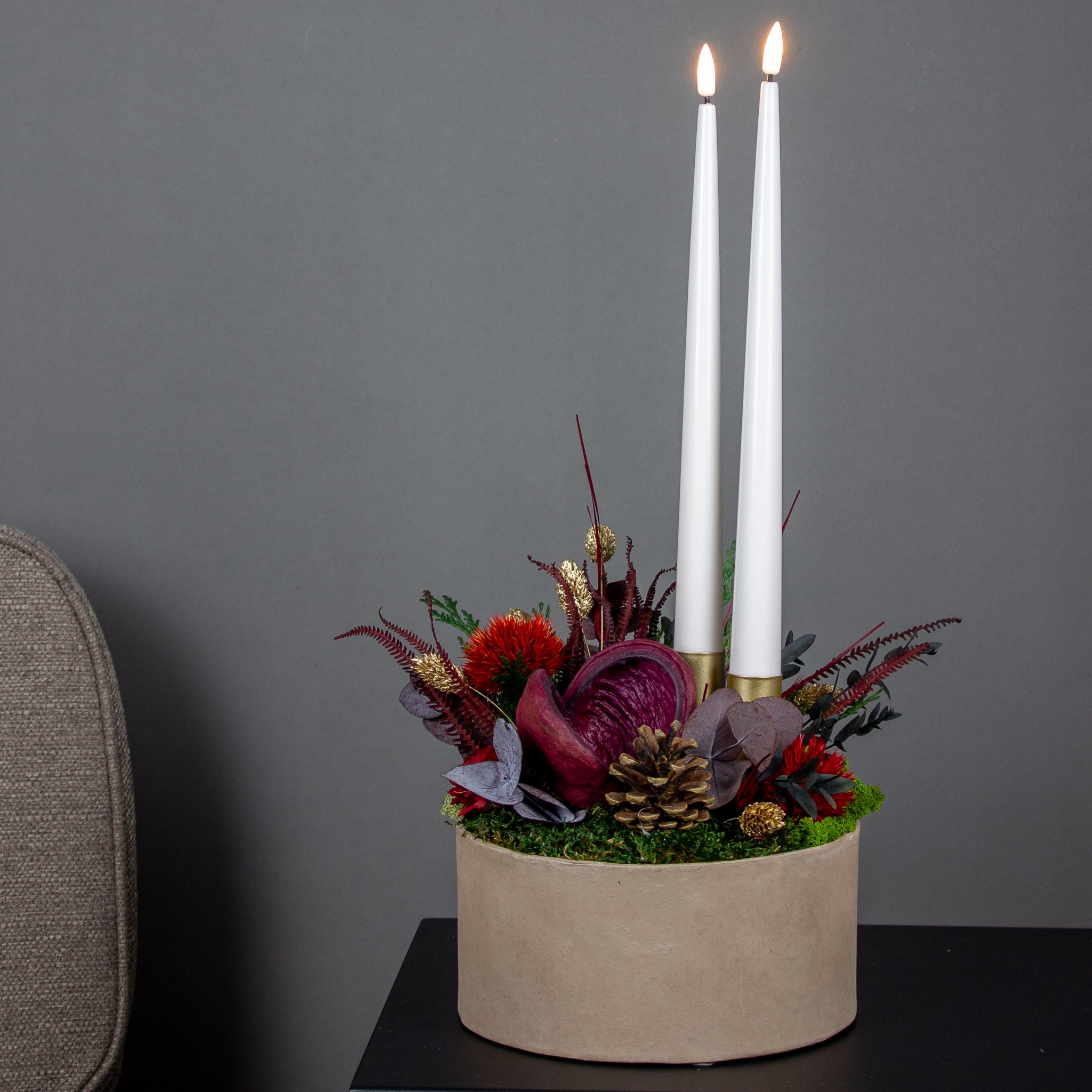 Juledekoration med røde blomster og to lys arrangeret i en skål.