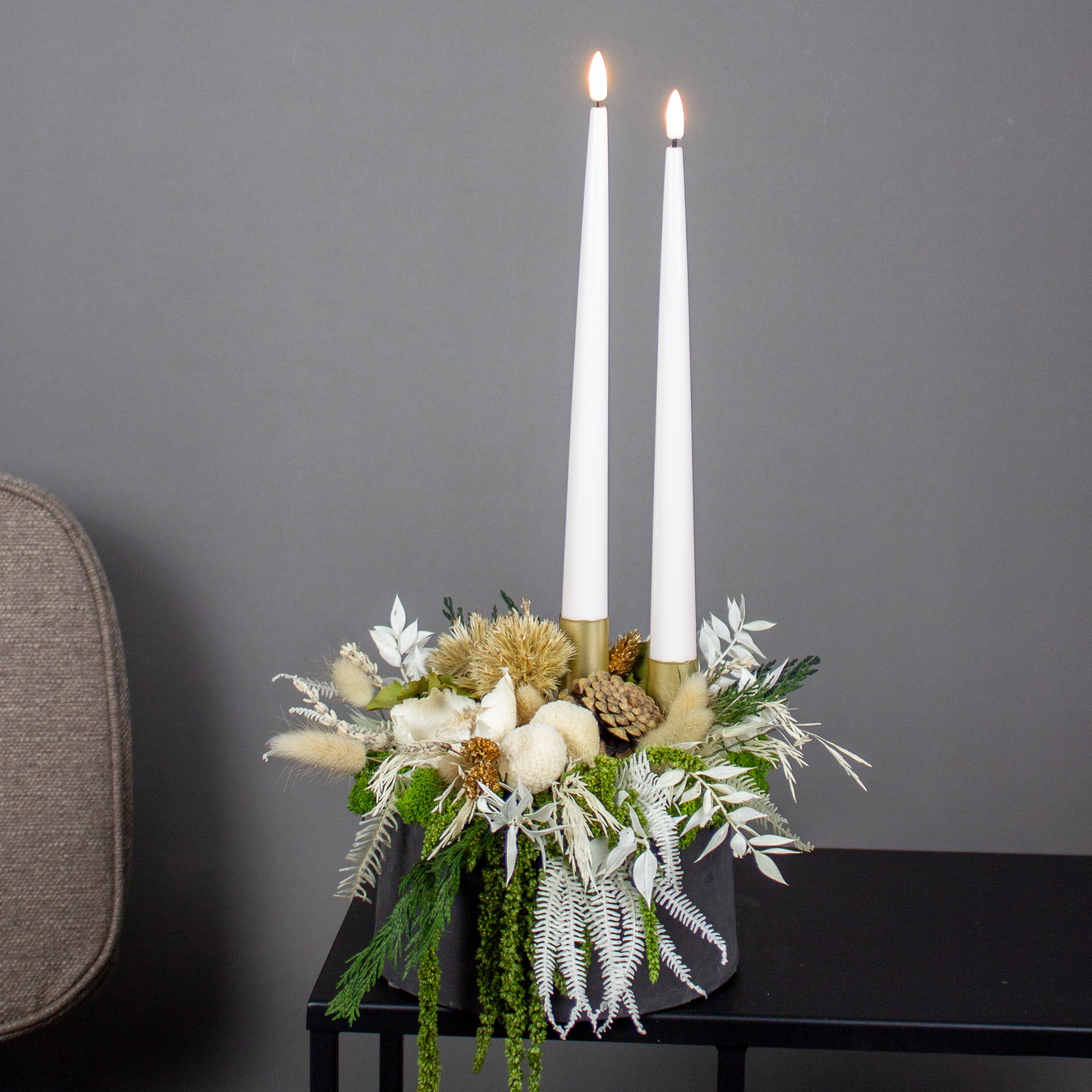 Juledekoration med lyse blomster og to lys arrangeret i en skål.