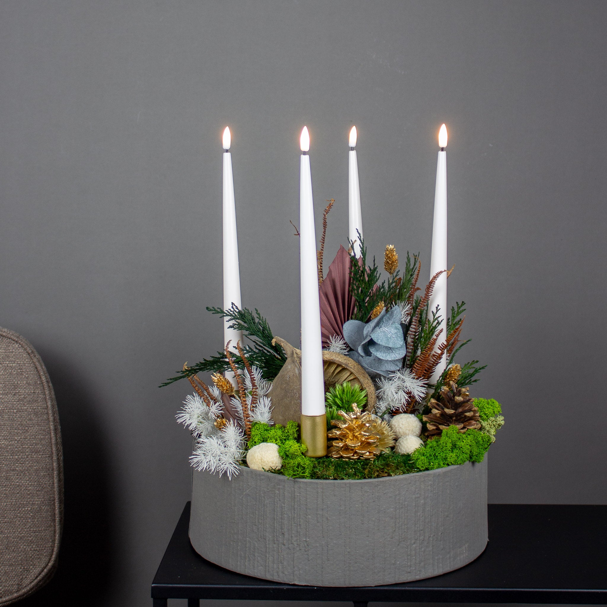 Juledekoration med langtidsholdbare blomster i brune og gyldne nuancer samt fire lys i en skål.