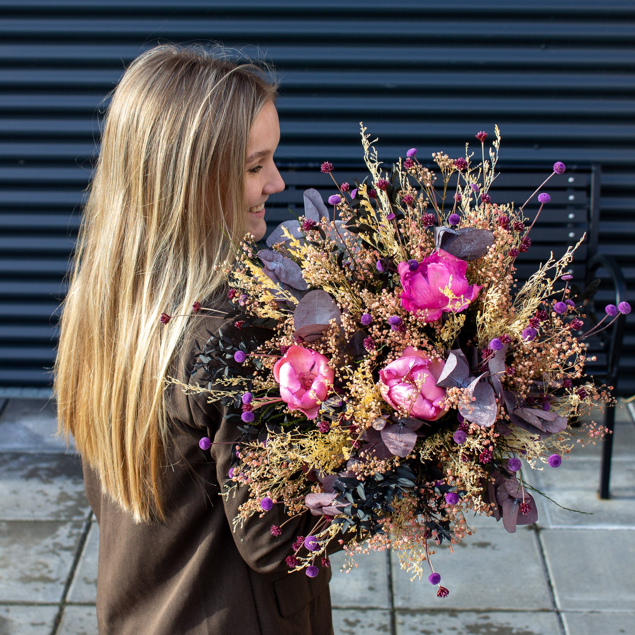 En smilende ung kvinde holder en stor blomsterbuket med pink accenter i armene