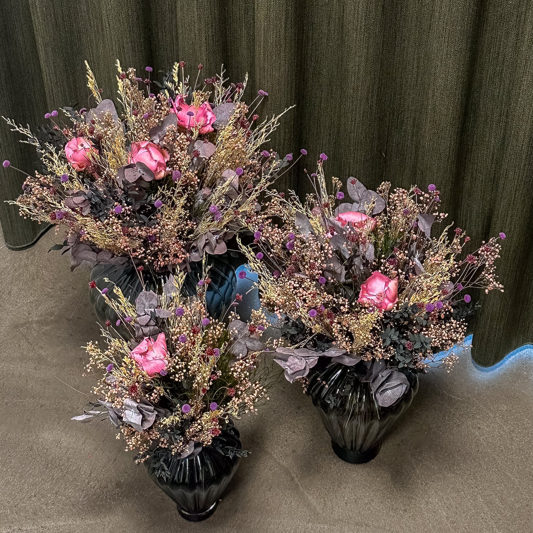 Tre langtidsholdbare buketter i forskellige størrelser står i glasvaser på gulvet.