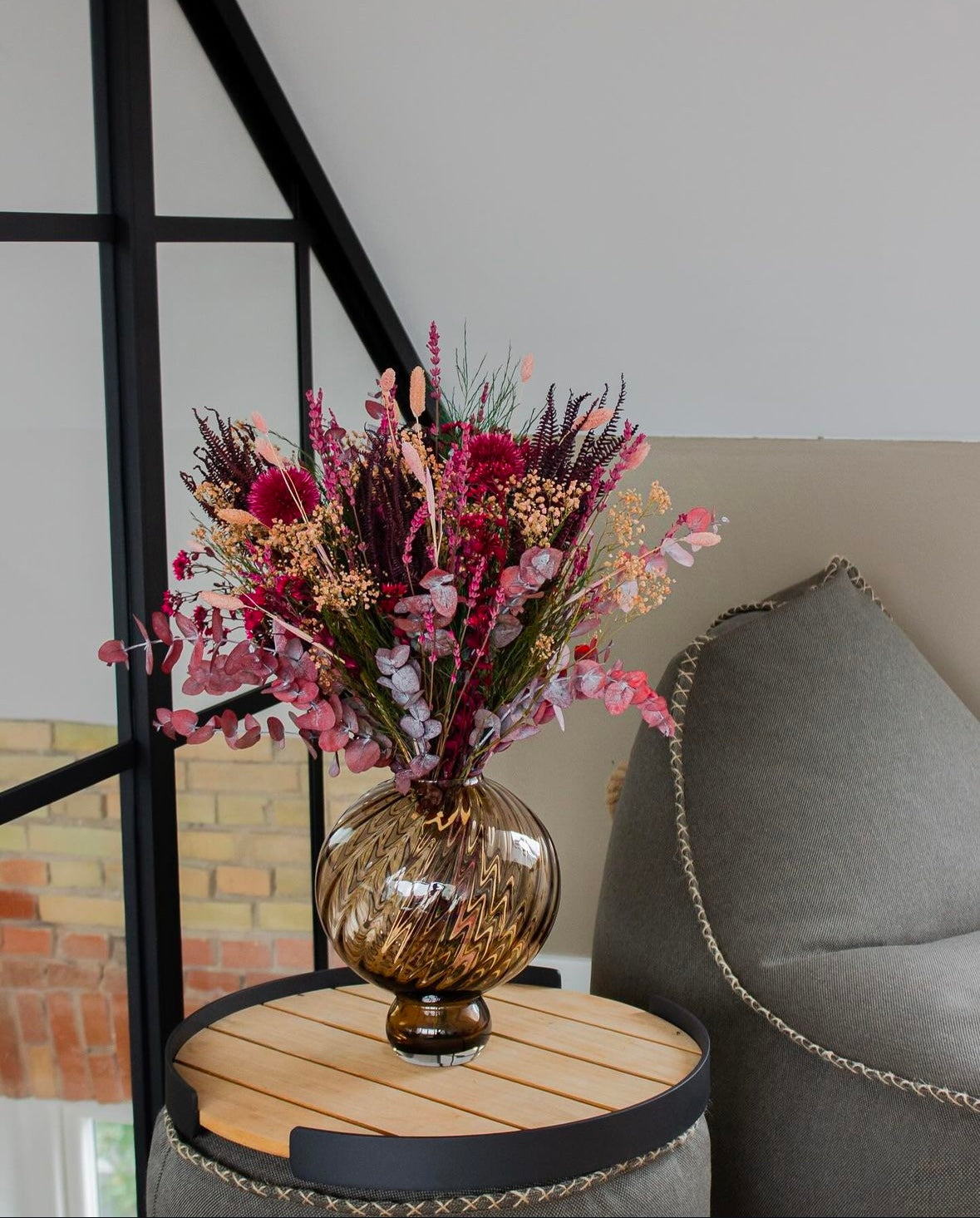 En buket med rød-pink accenter står på et sidebord.