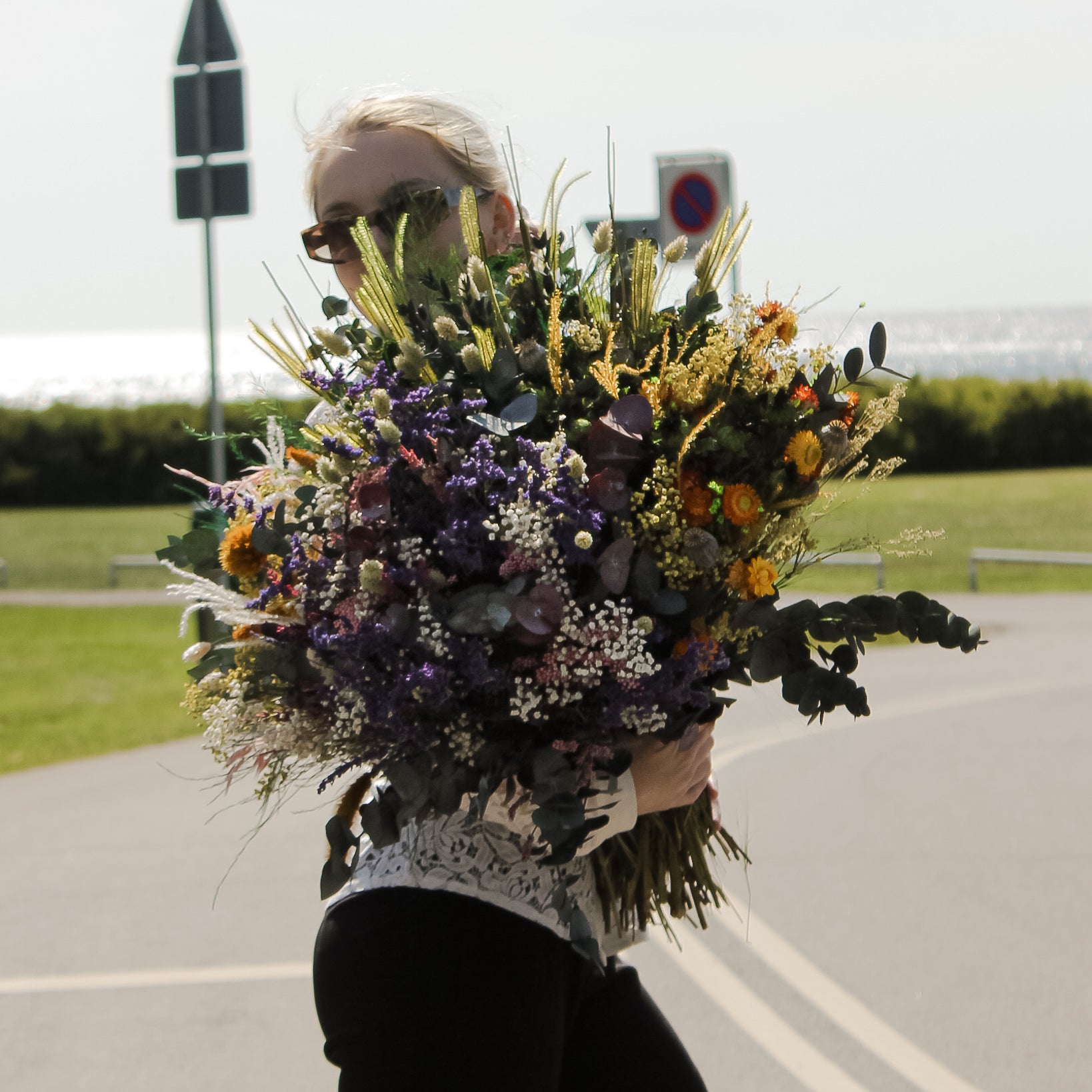 En ung kvinde holder en fyldig buket i orange og lilla nuancer i armene.