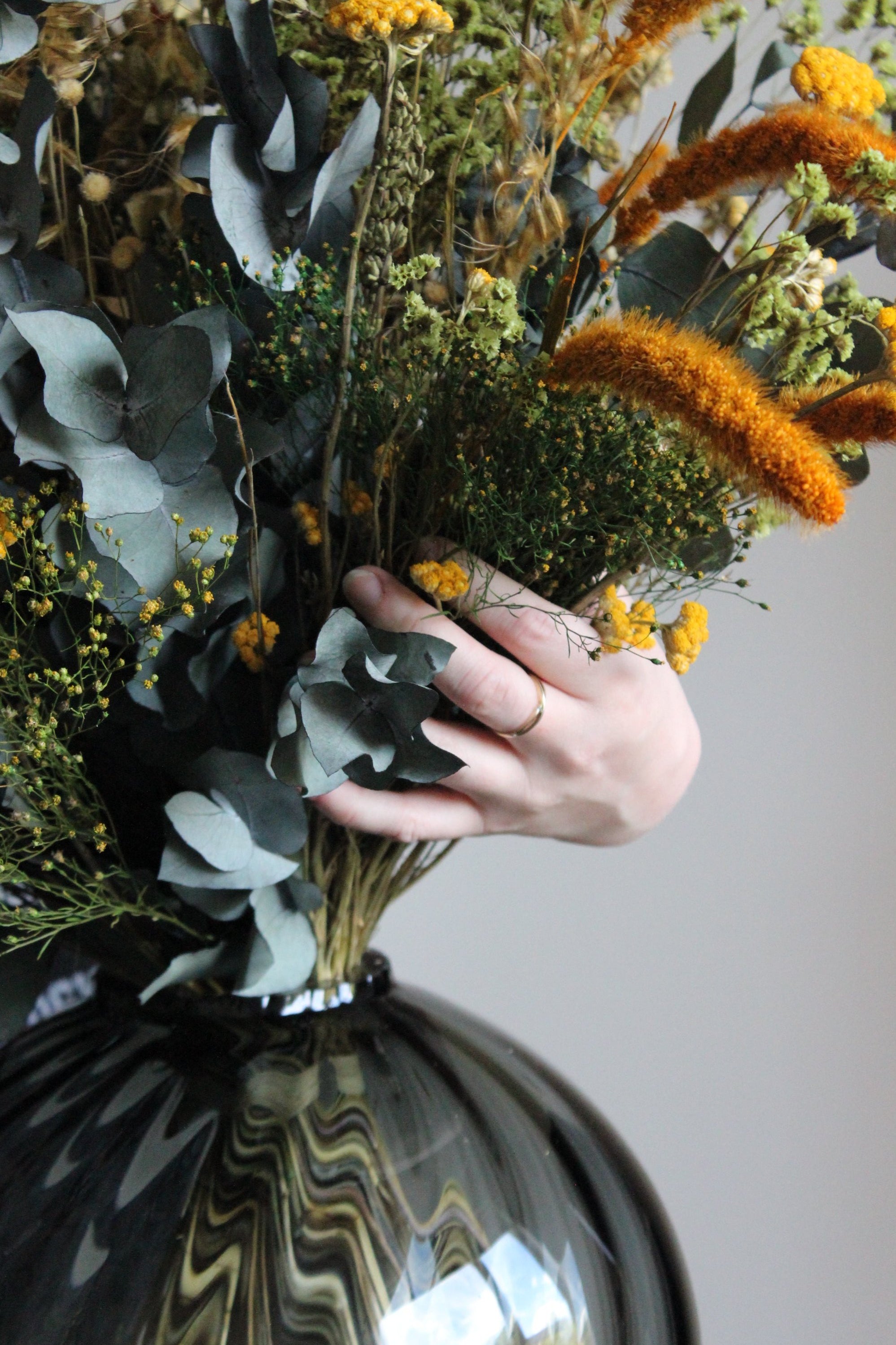 Nærbillede af en buket i varme efterårsfarver, som arrangeres i en rund glasvase af en kvinde.