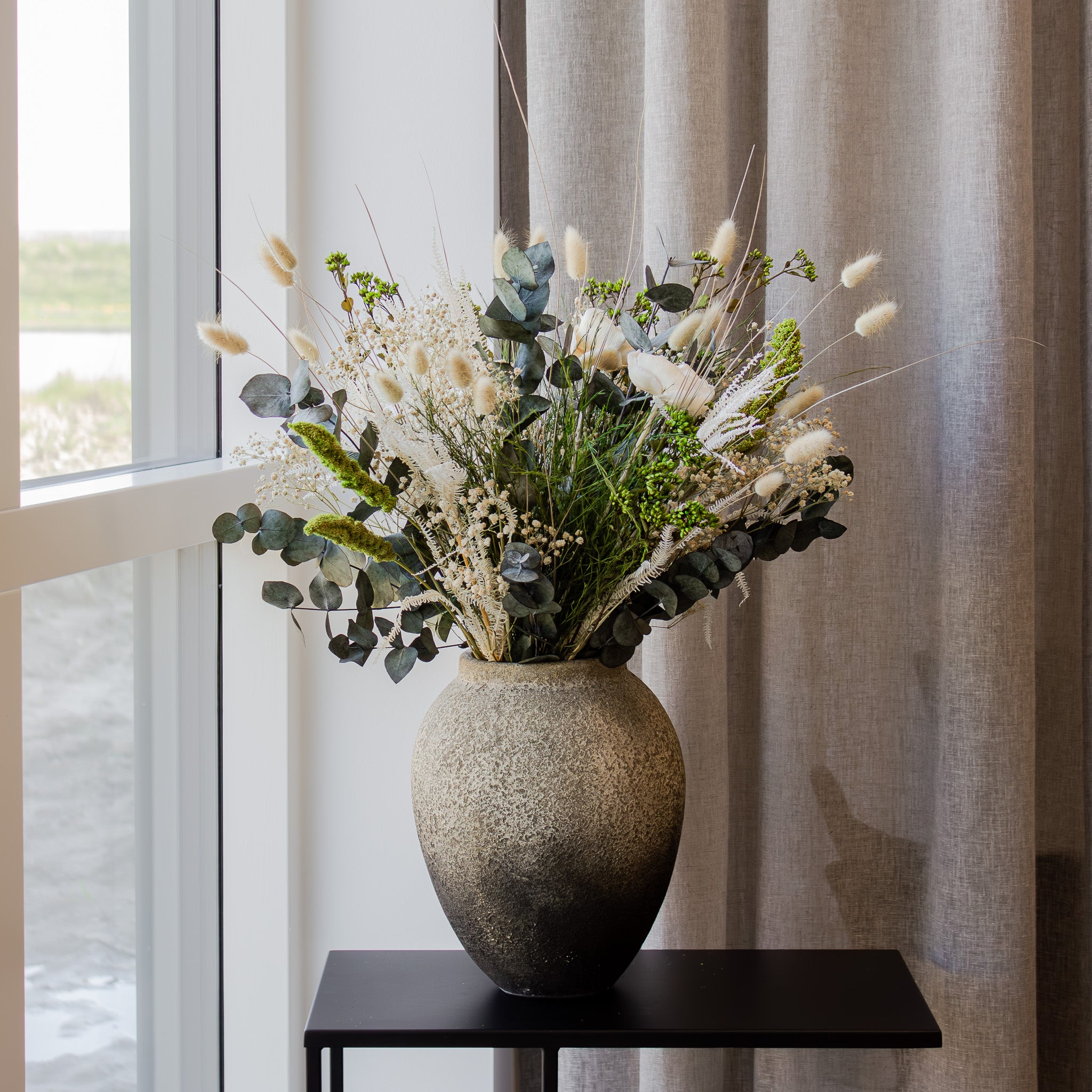 En fyldig grÞn-hvid buket stÄr i en terracottavase.