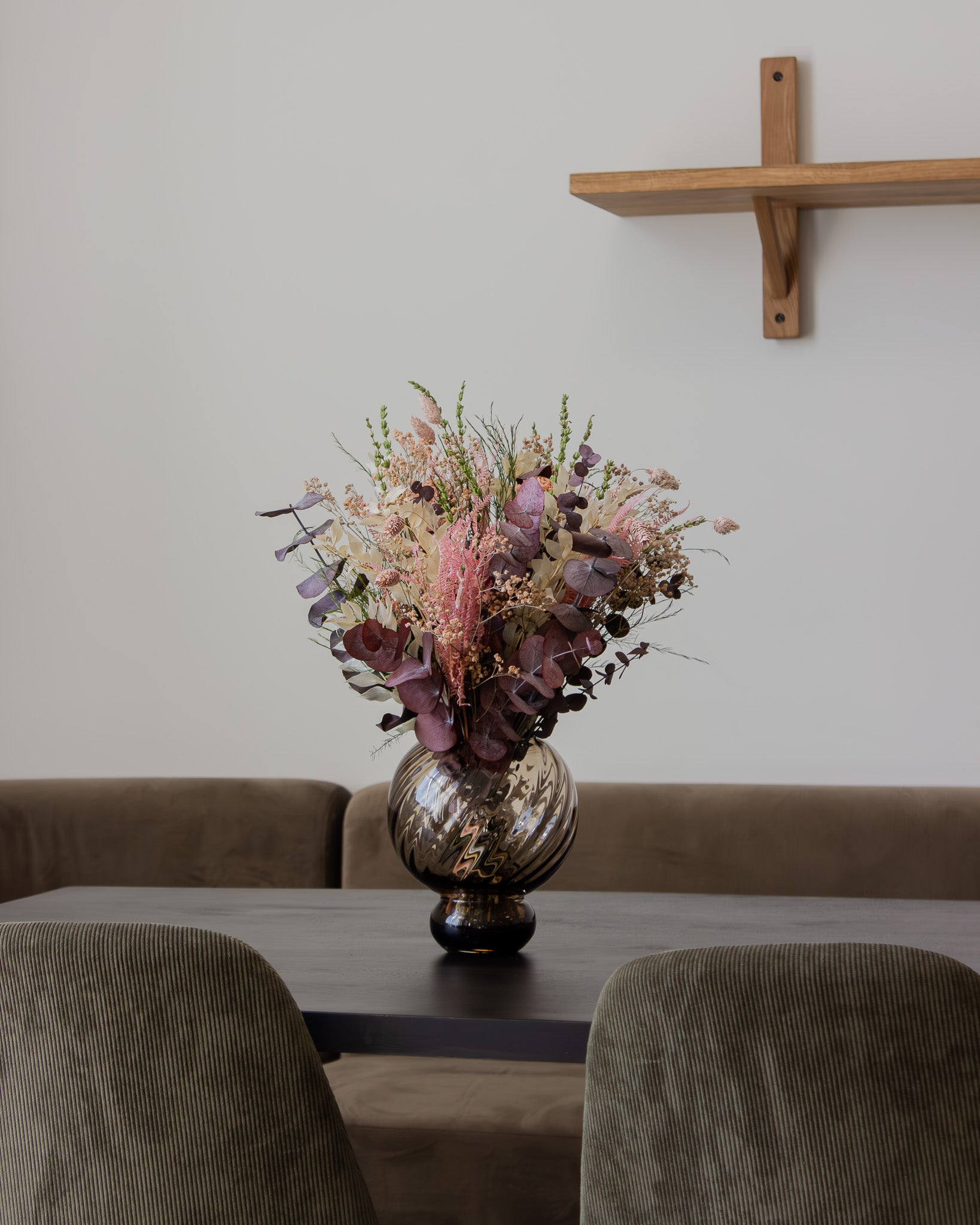 På bordet i en siddegruppe står en blomsterbuket i bløde rosa nuancer i en rund glasvase.