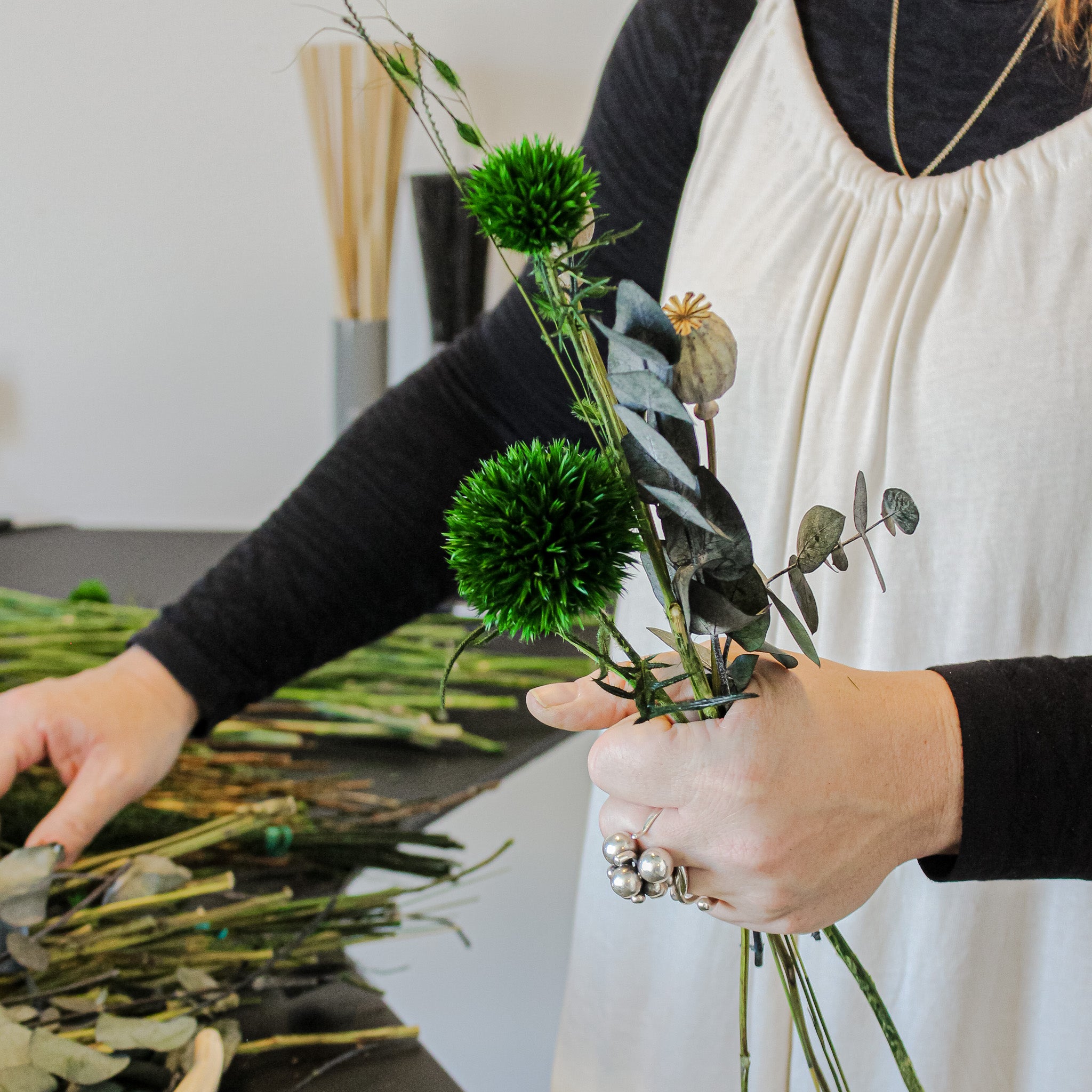 Eine Floristin hält mehrere Blumenstiele in der linken Hand, während sie mit der rechten Hand nach weiteren greift.