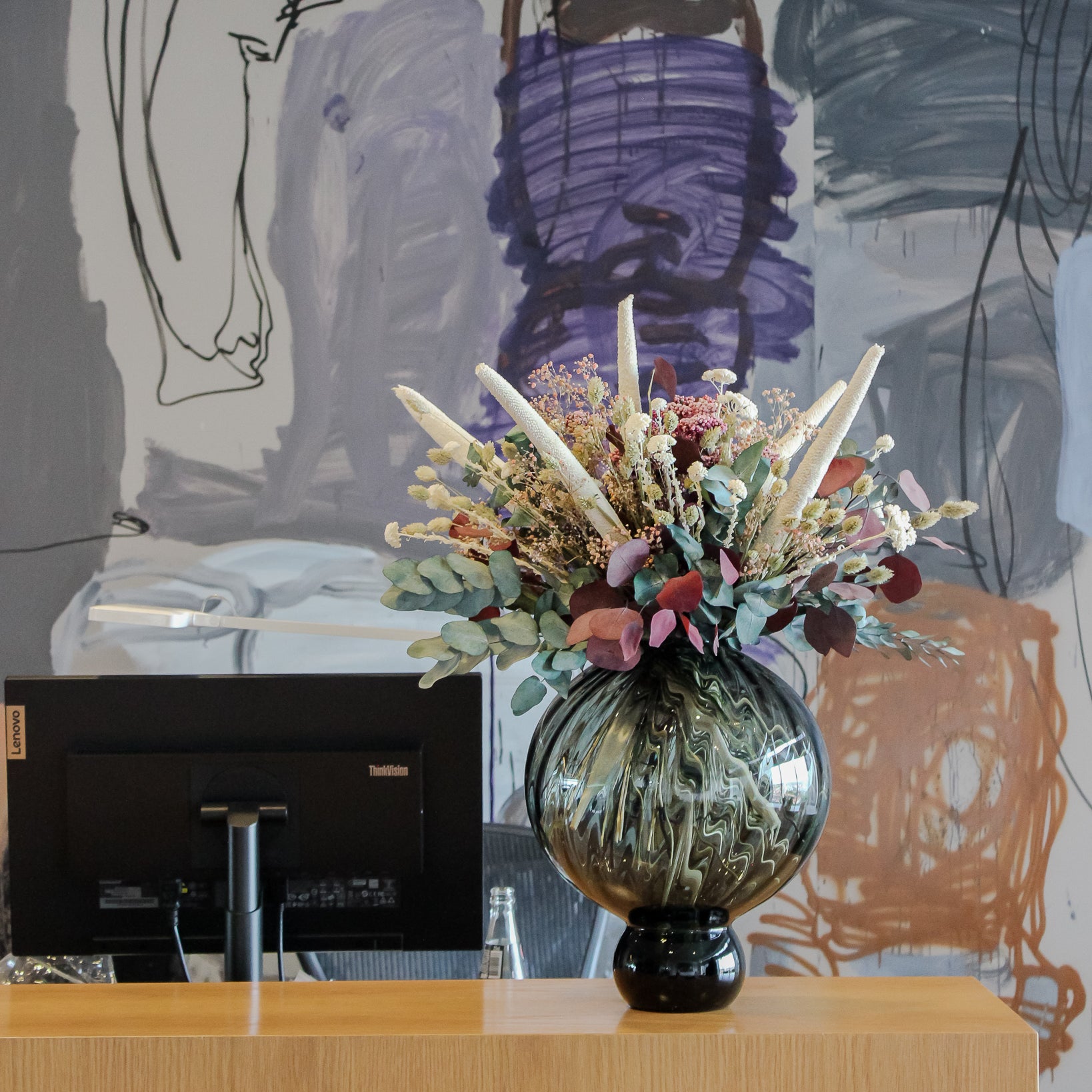 På et skrivebord står en rund vase med iøjnefaldende blomster.