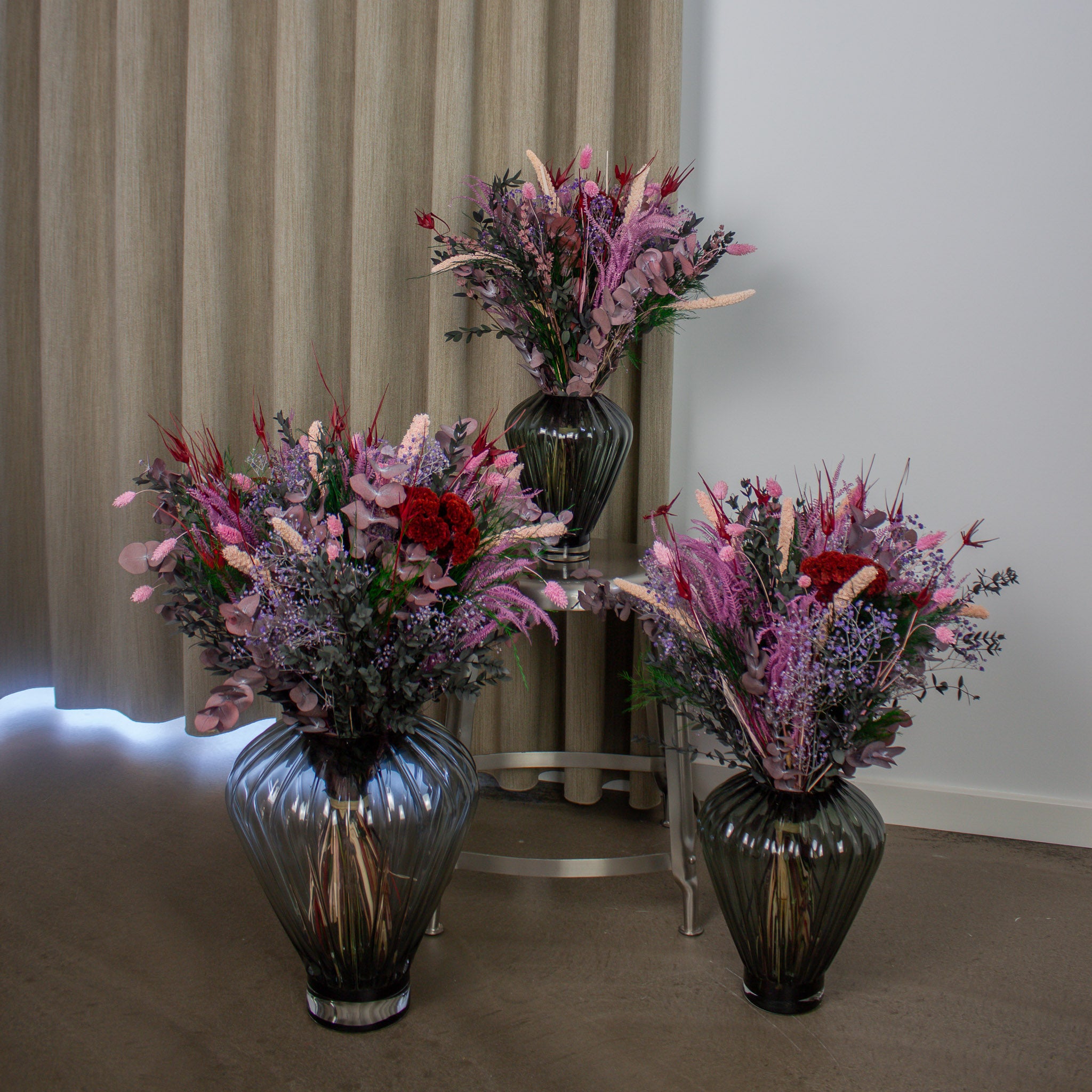 Tre blomsterbukke i forskellige størrelser står i rippede glasvaser, der matcher buketternes størrelse.