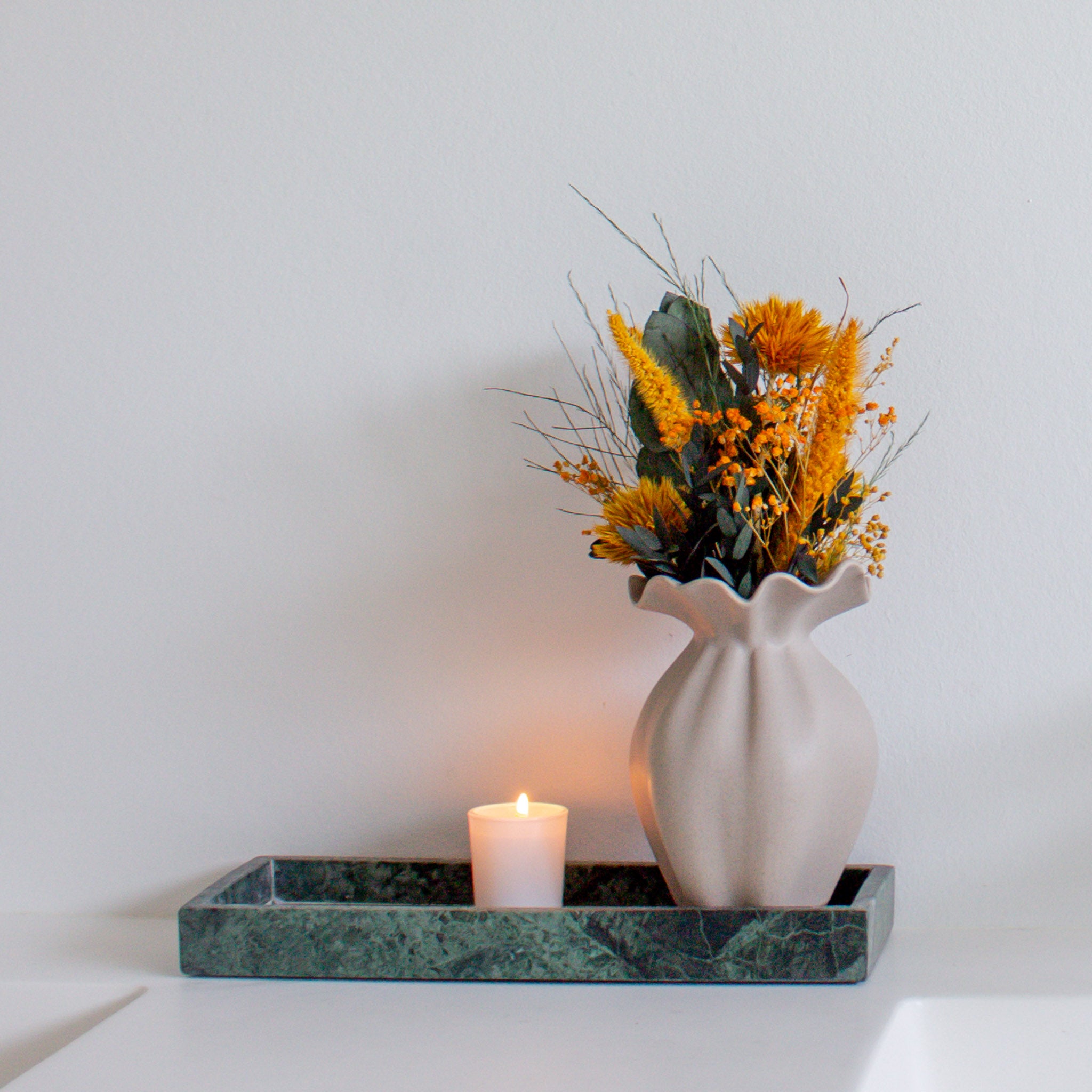 På et fad står en lille vase med en mini-buket i kraftige orange nuancer.