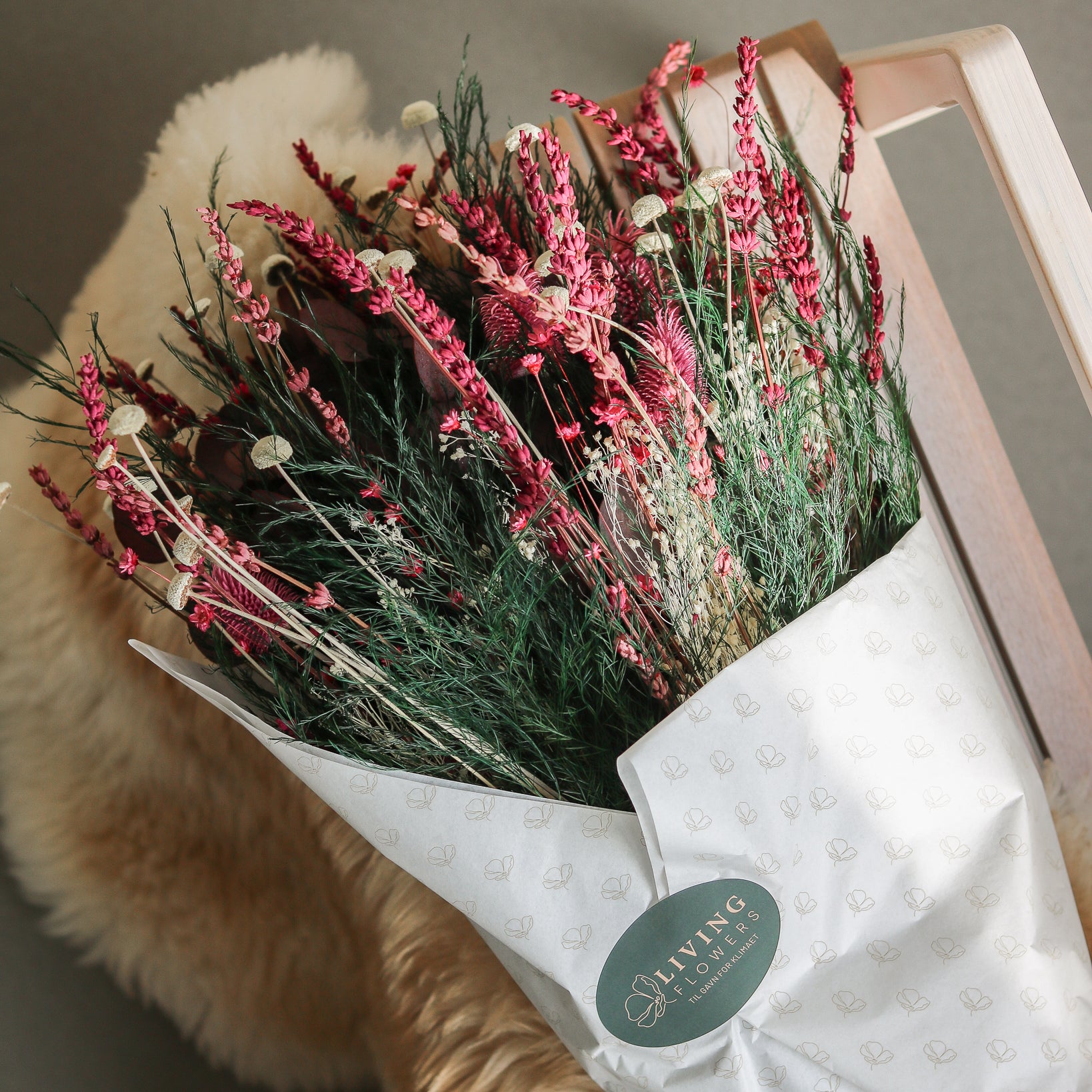 På en stol ligger en blomsterbuket i røde nuancer med hvide highlights, indpakket i silkepapir.