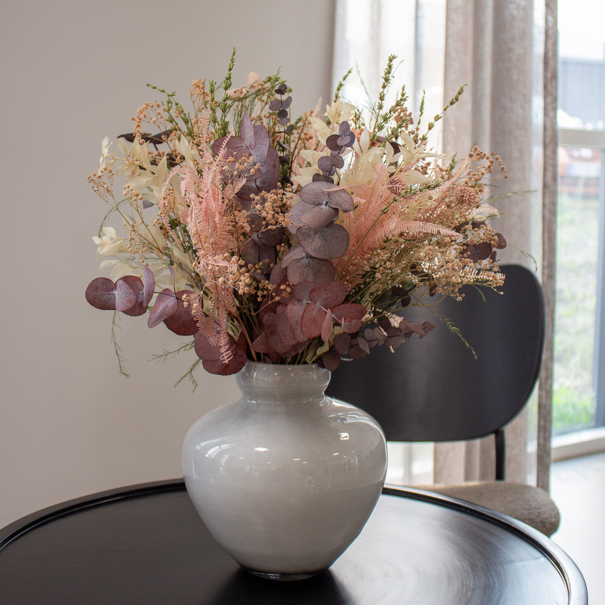 På et bord står en vase af hvidt mælkeglas, hvor en sart lyserød blomsterbuket står.