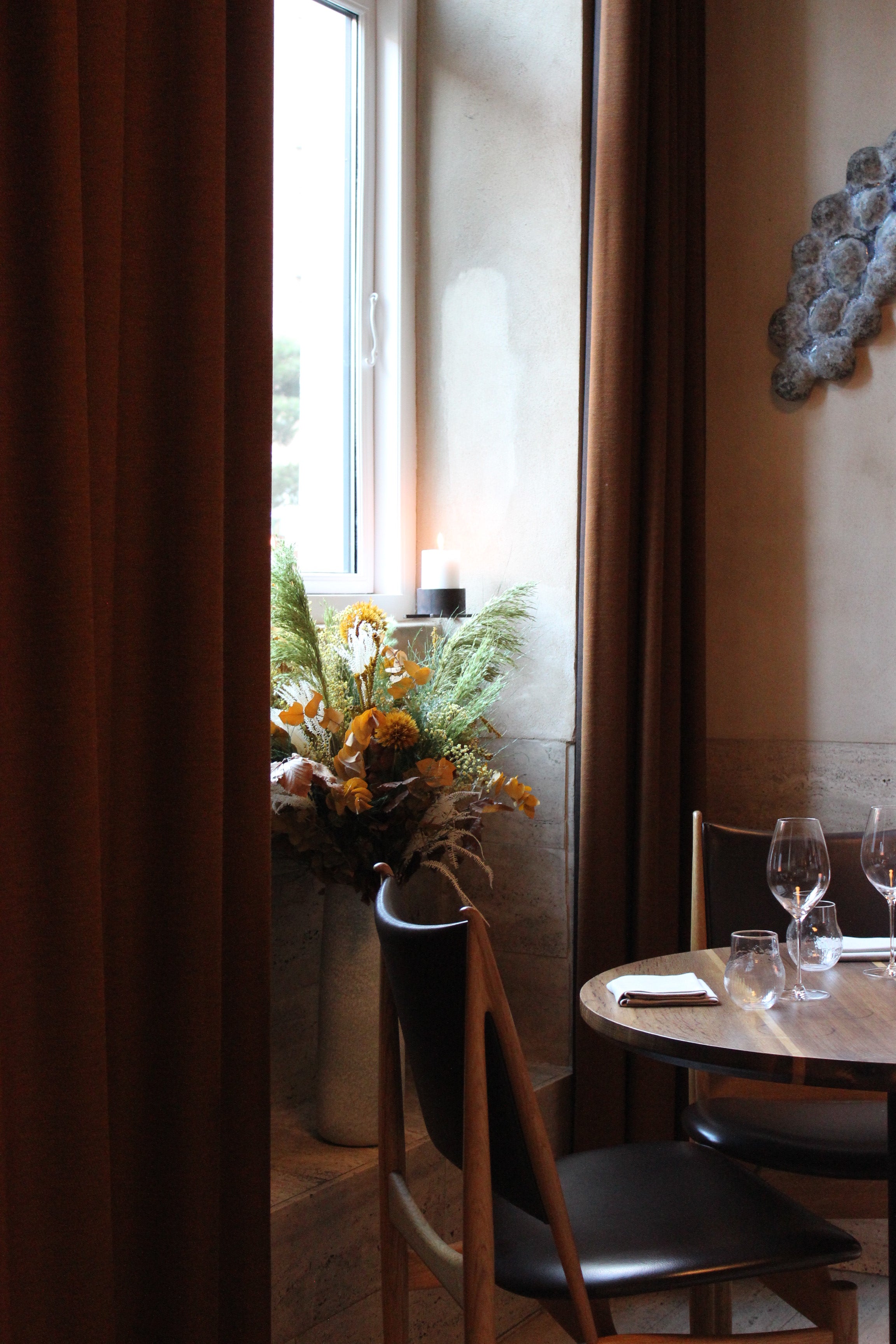 I en vinduesniche står en buket i varme efterårsfarver ved siden af et smukt dækket bord.