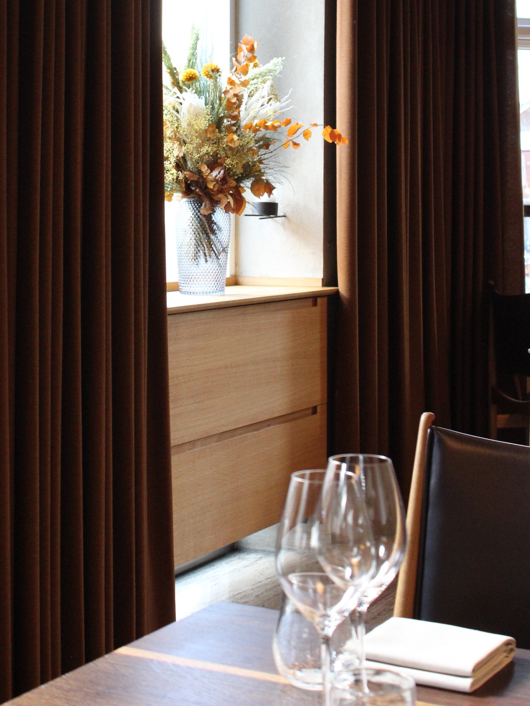 I en stemningsfuld restaurant står en langtidsholdbar blomsterbuket i varme efterårsfarver på vindueskarmen.