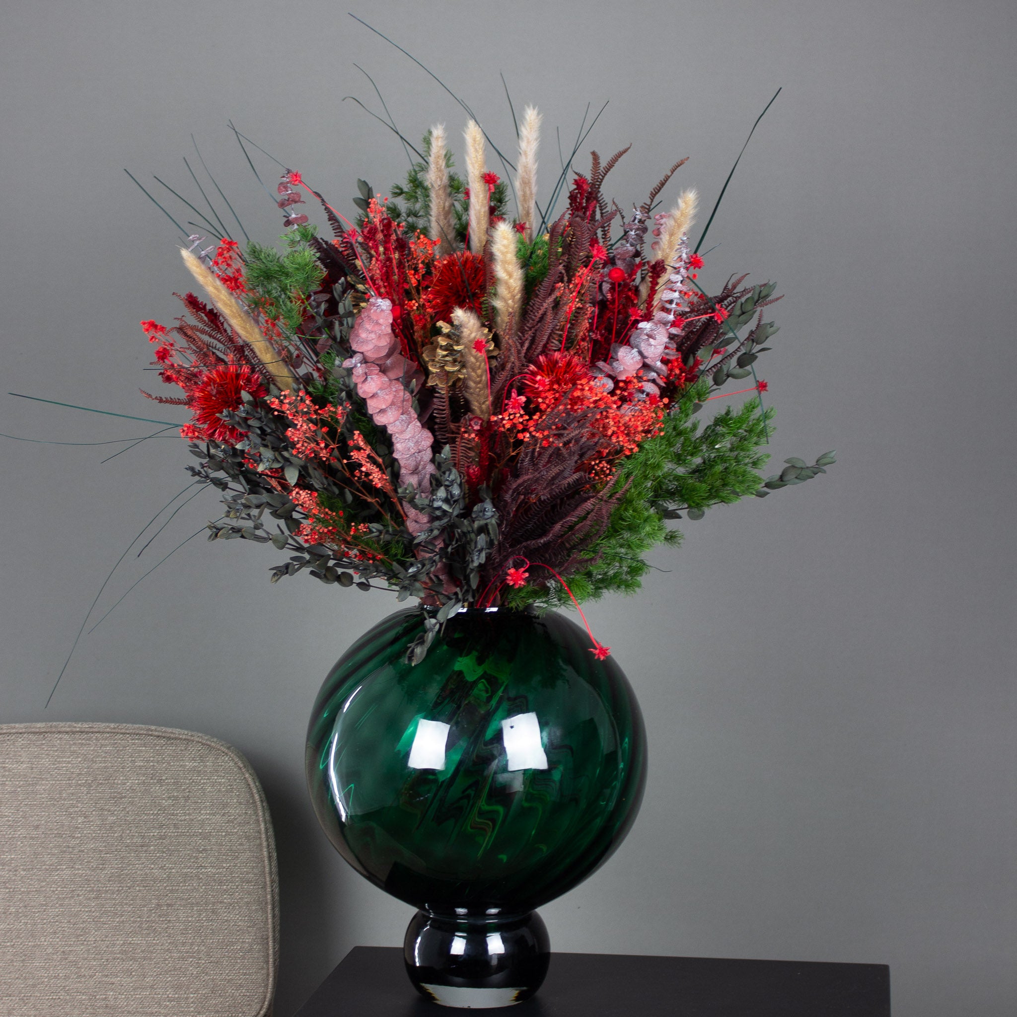 En fyldig grøn-rød buket står i en rund glasvase.