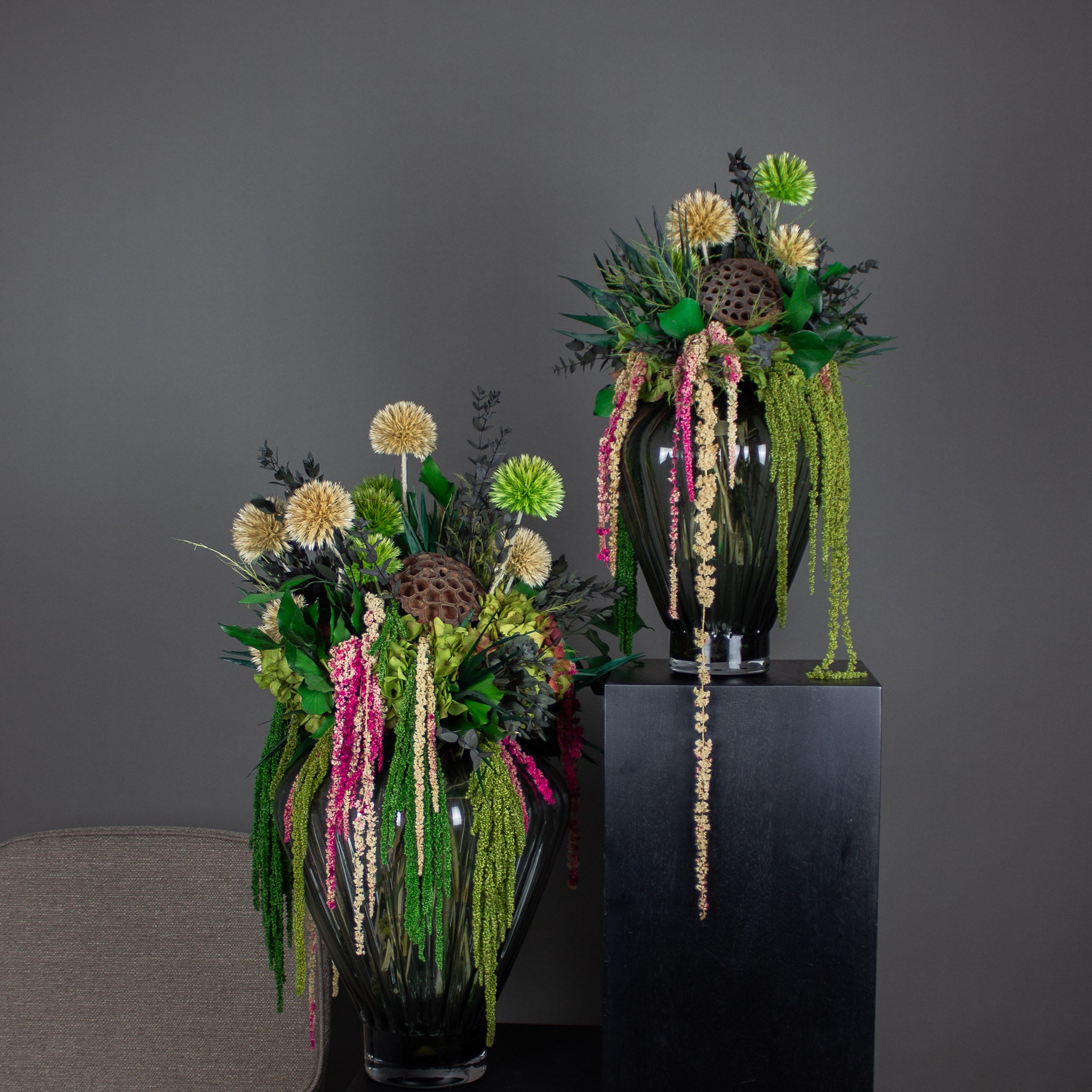 To unikke buketter i grønne og pink nuancer med hængende elementer står på podier.