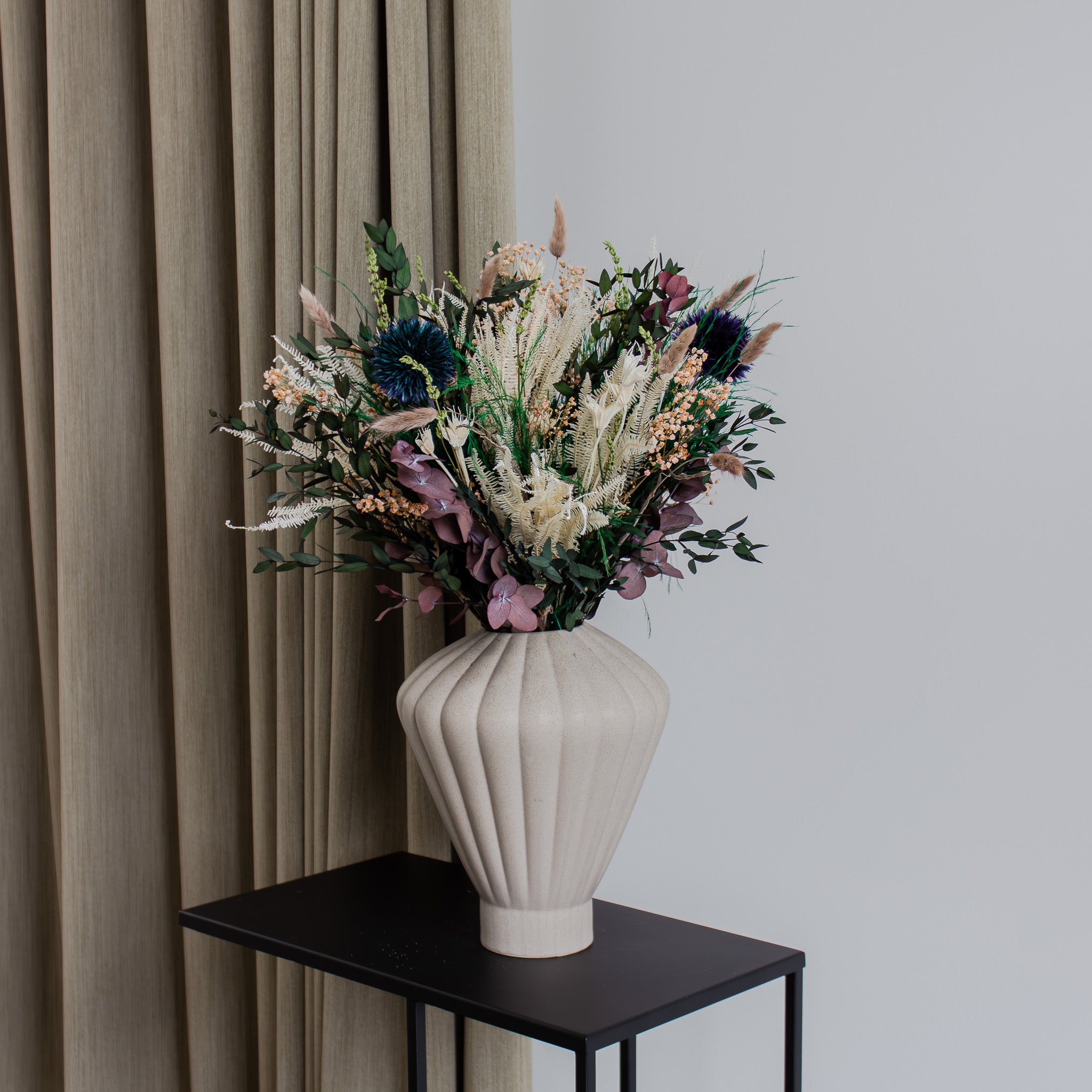 På et sidebord står en blomsterbuket i sarte farver med lilla accenter.