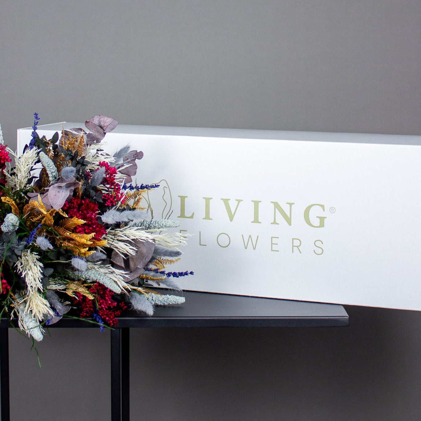 FĂždselsdagsbuket En langtidsholdbar buket i dybe vinterfarver ligger foran en hvid forsendelseskasse.