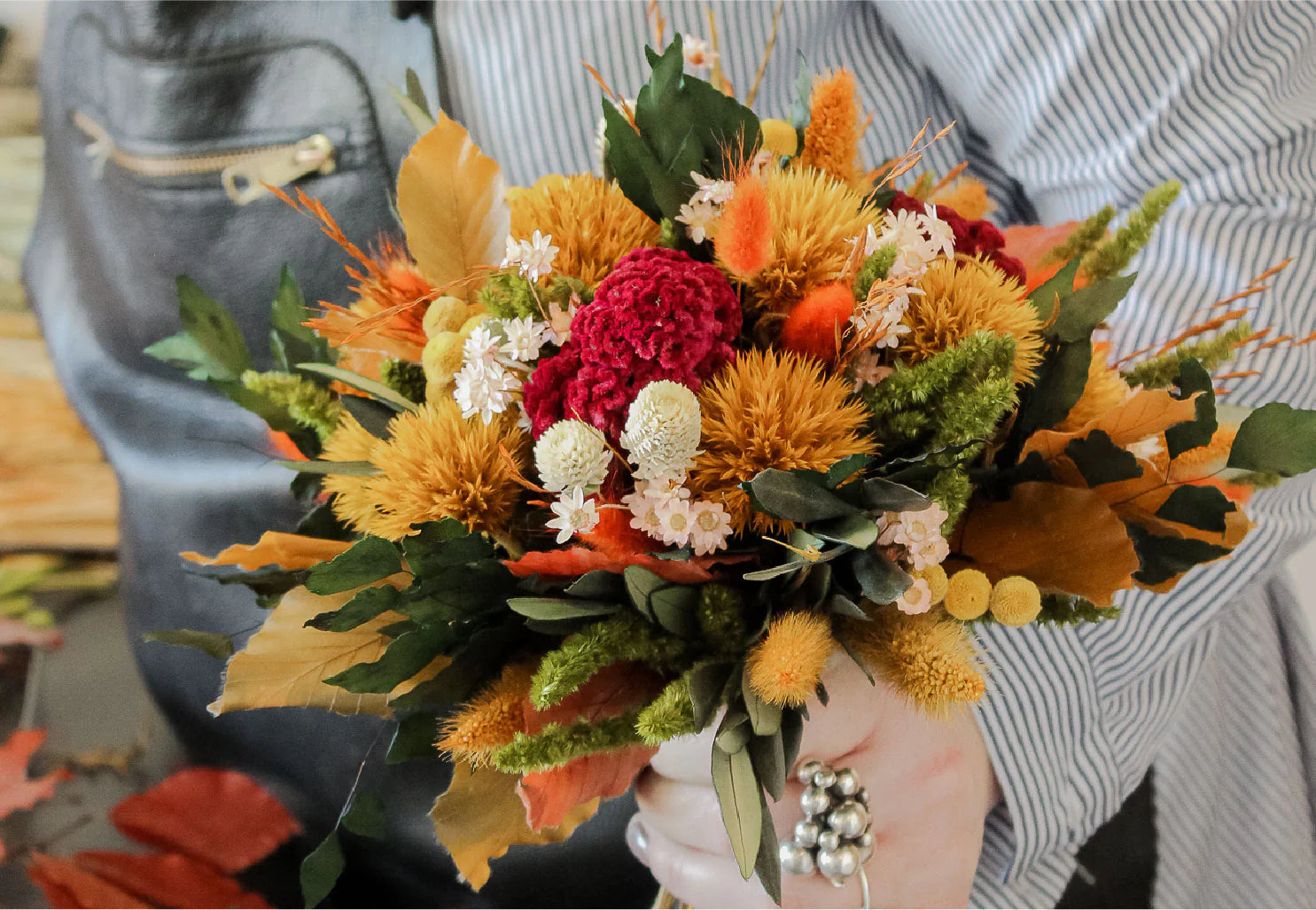 En kvinde holder en lille blomsterbuket i efterårsagtige orange og røde nuancer.