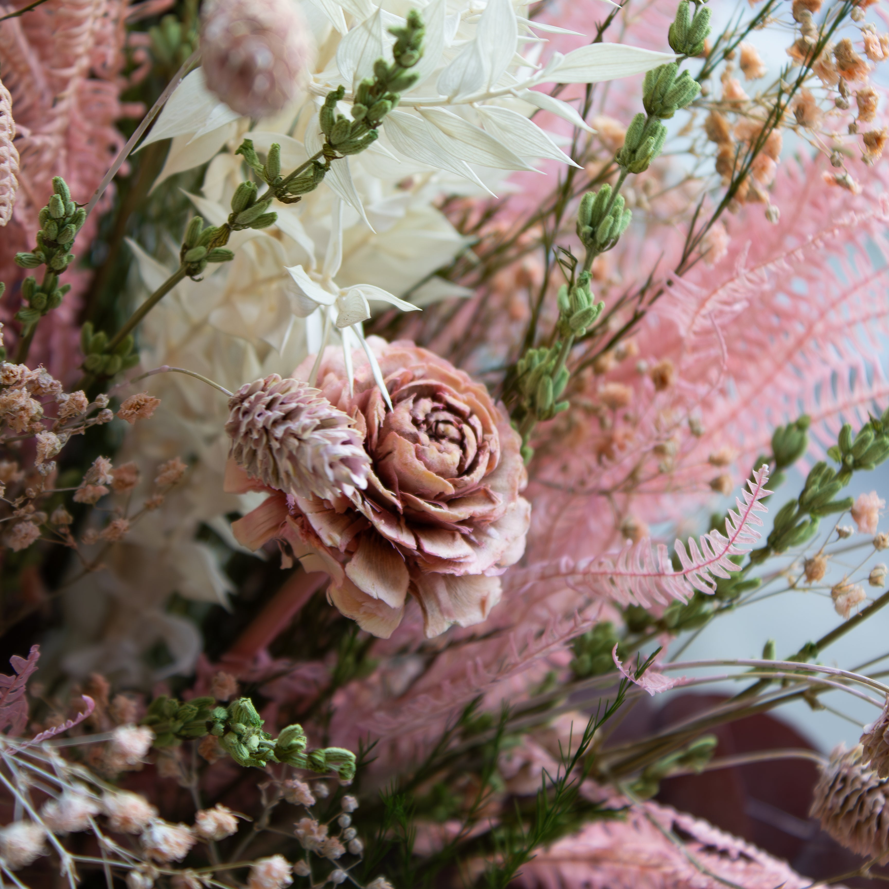 Nærbillede af en blomsterbuket med langtidsholdbare blomster i sarte lyserøde nuancer.
