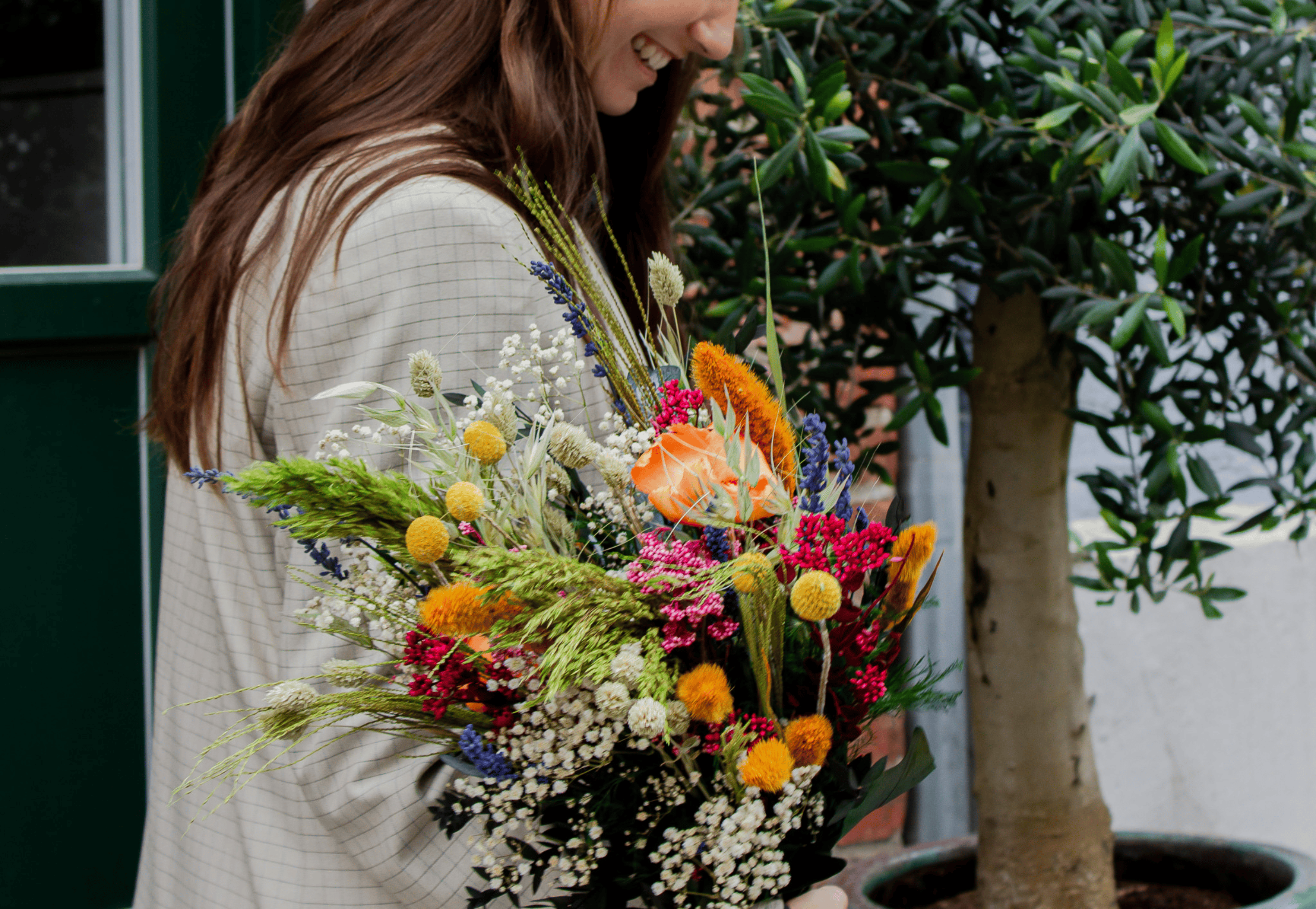 En smilende kvinde holder en farverig blomsterbuket i hånden.