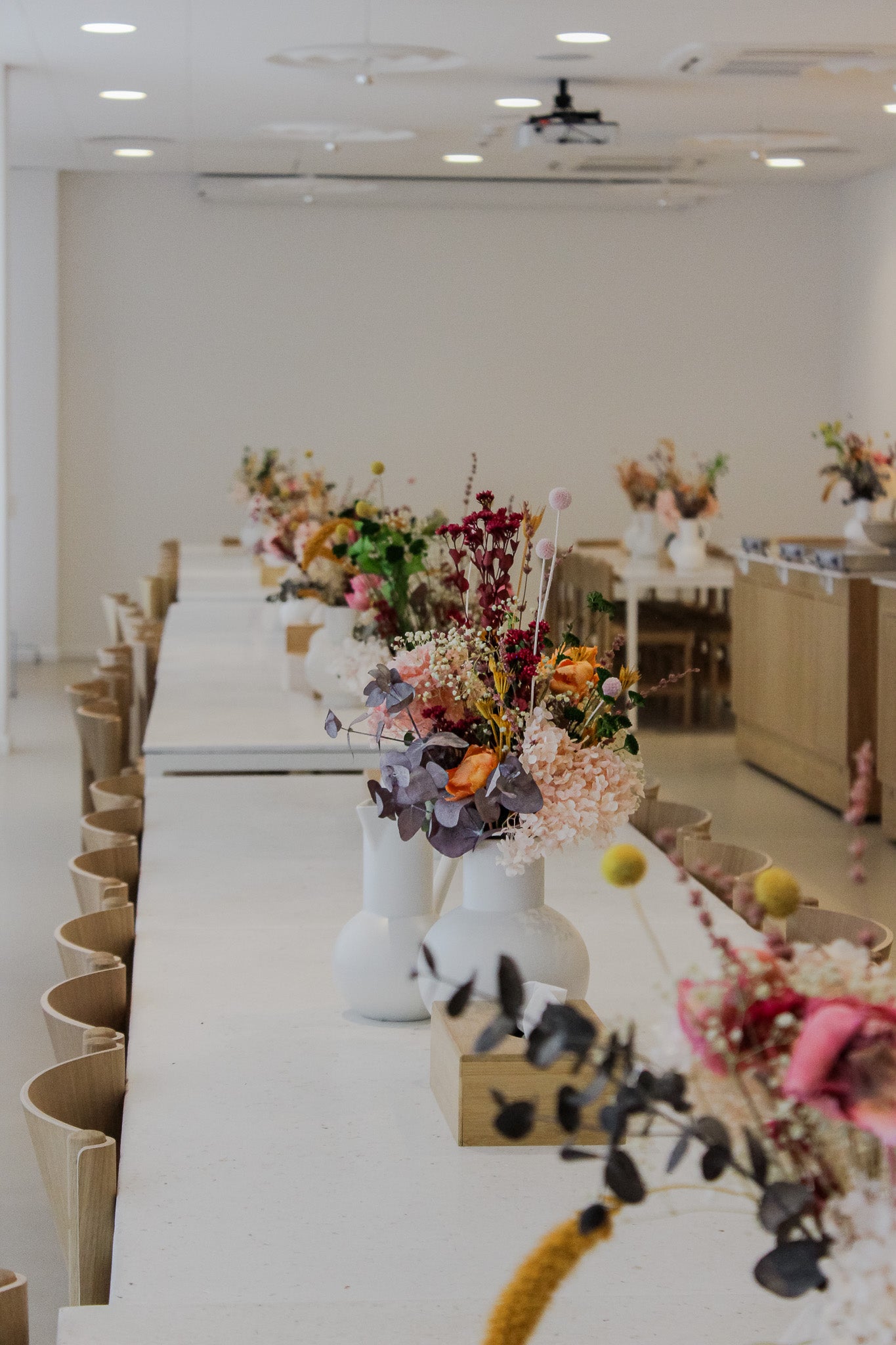 På et langt bord i et pauserum står mange små vaser med langtidsholdbare blomster.