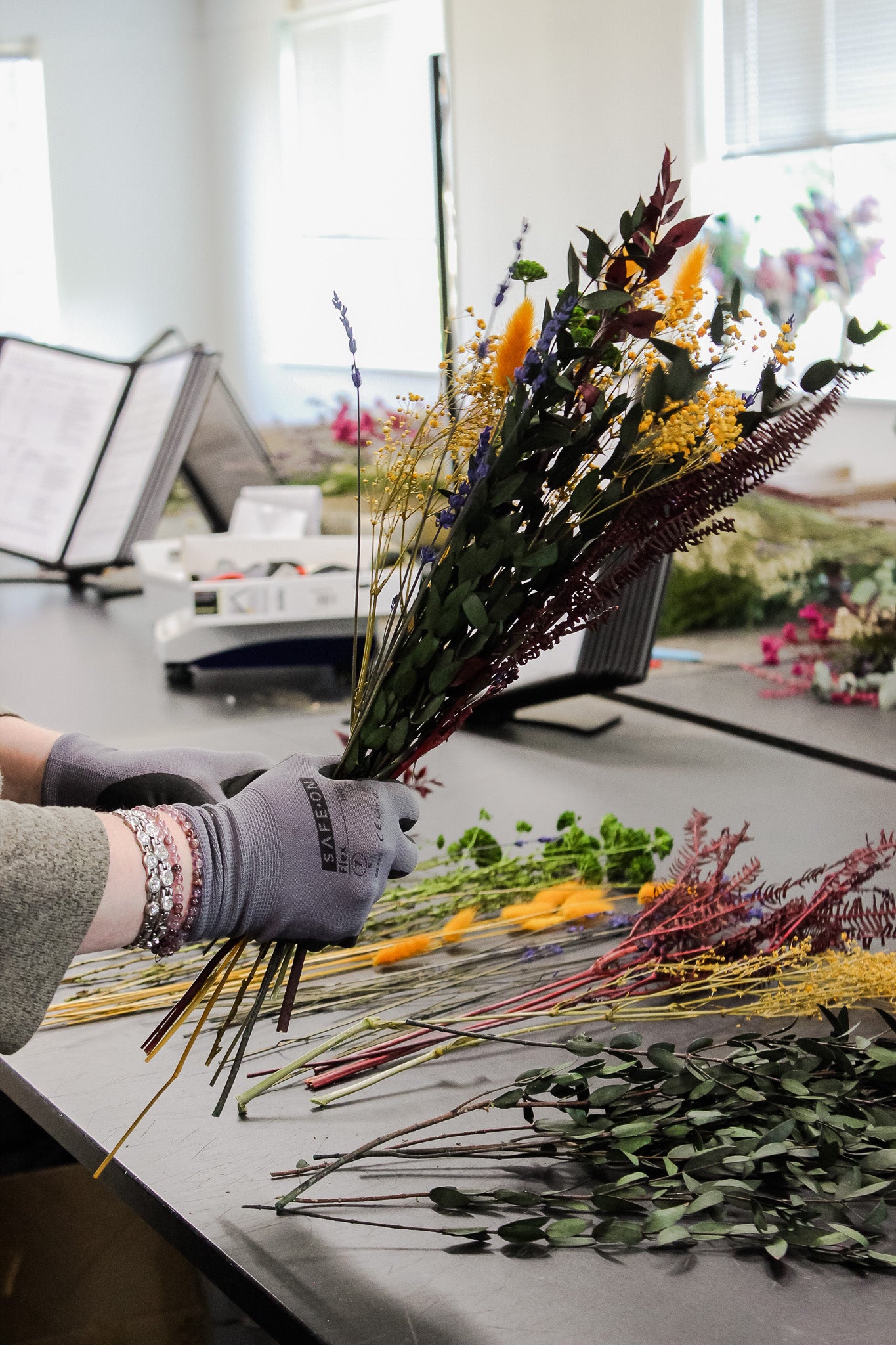 En florist binder en buket af langtidsholdbare blomster i varme farver.