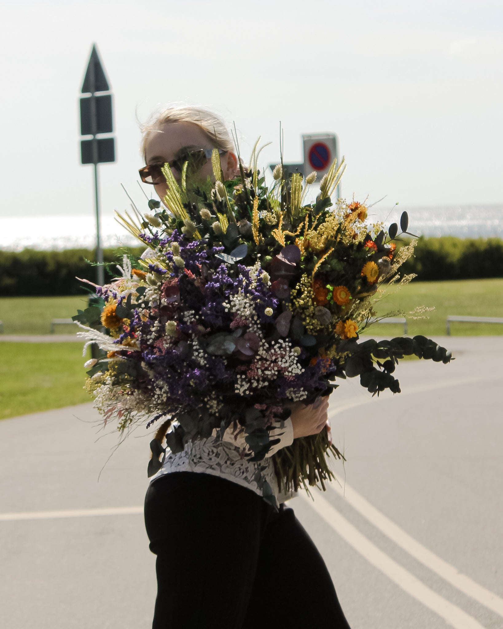 En ung kvinde holder en fyldig buket i orange og lilla nuancer i armene.