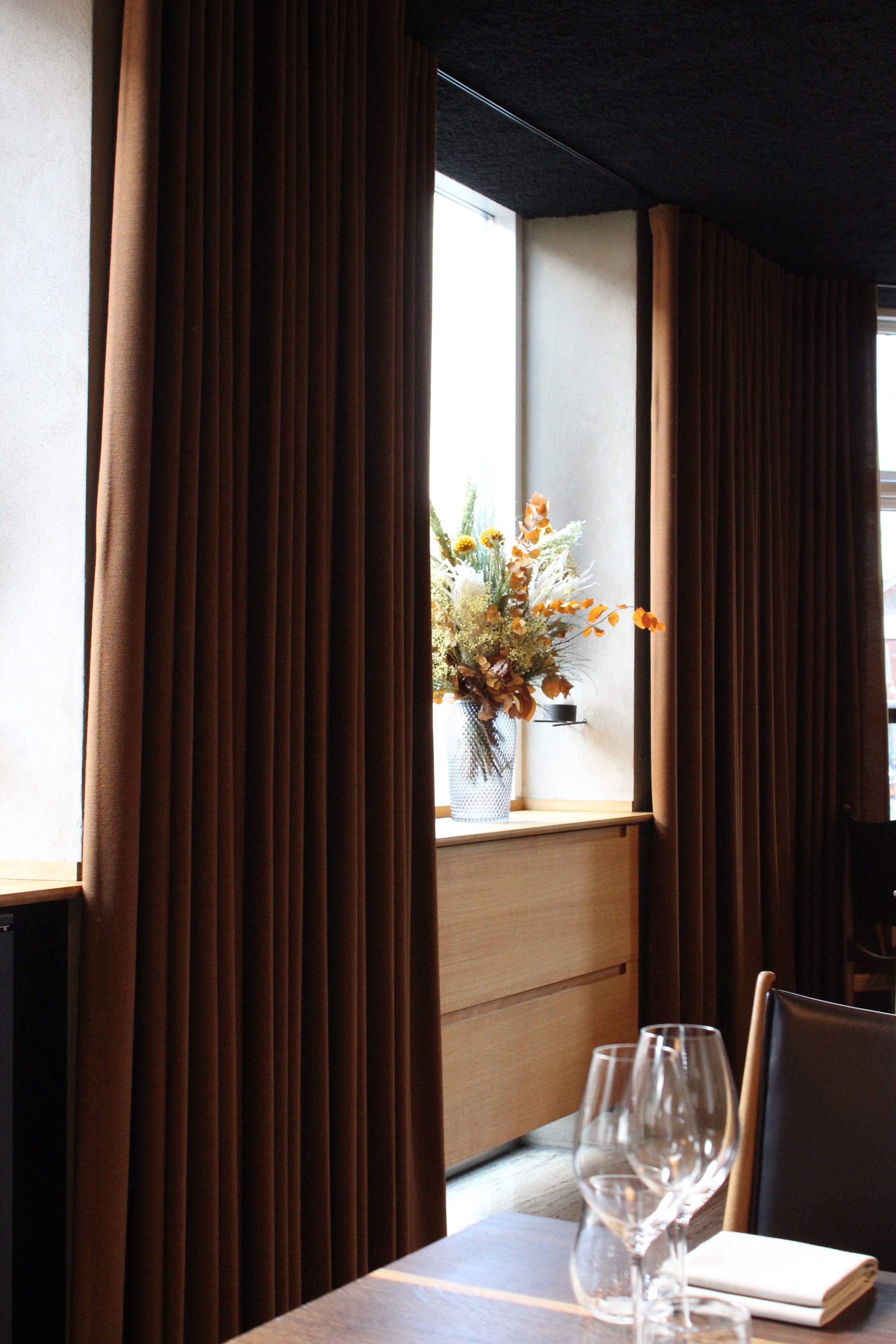 I en stemningsfuld restaurant står en langtidsholdbar blomsterbuket i varme efterårsfarver på vindueskarmen.