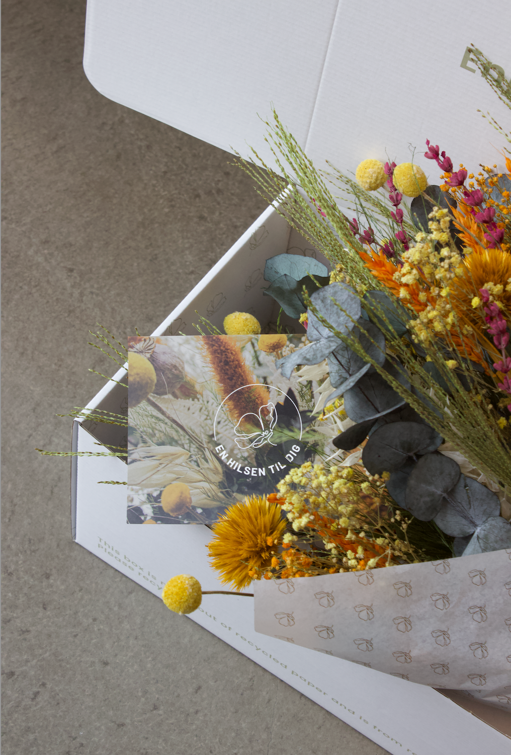 I en hvid kasse ligger en farverig buket sammen med et kort.