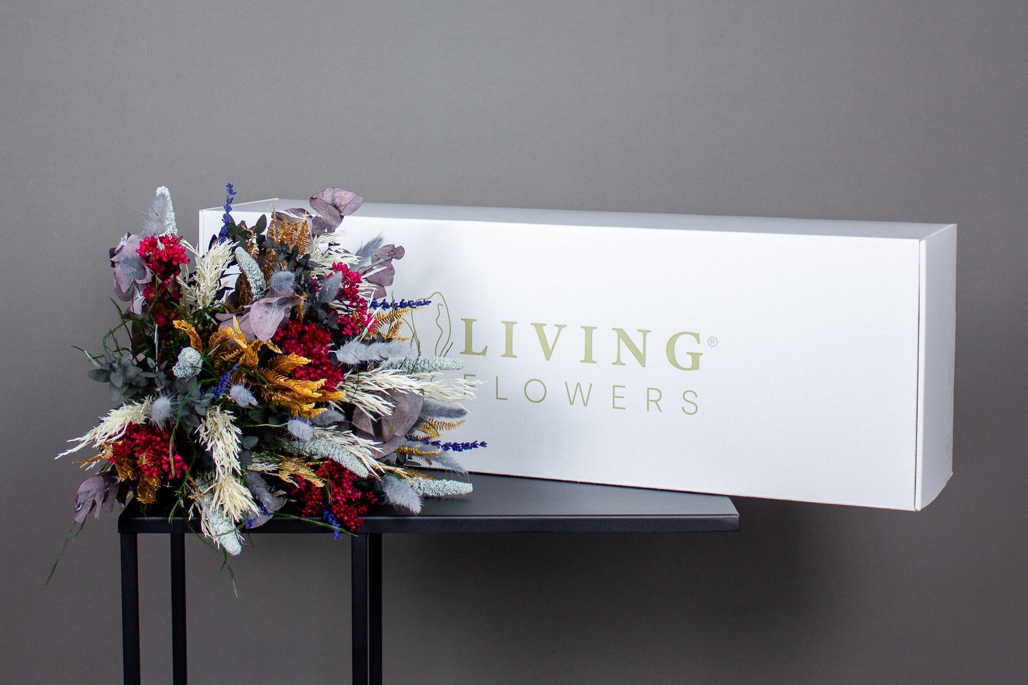 Fødselsdagsbuket En langtidsholdbar buket i dybe vinterfarver ligger foran en hvid forsendelseskasse.